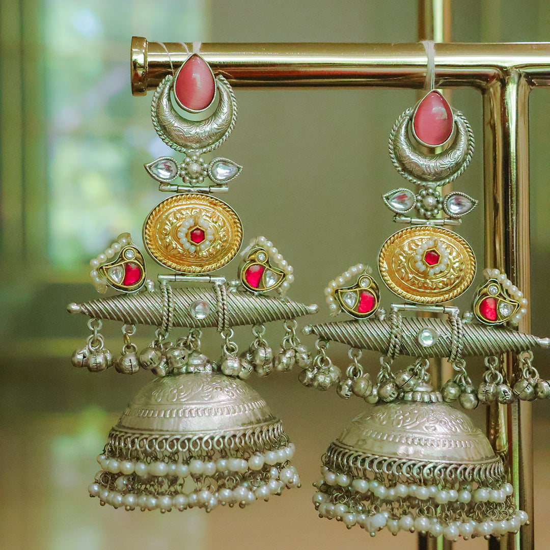 Ornate gold and silver earrings with red stones on a stand.
