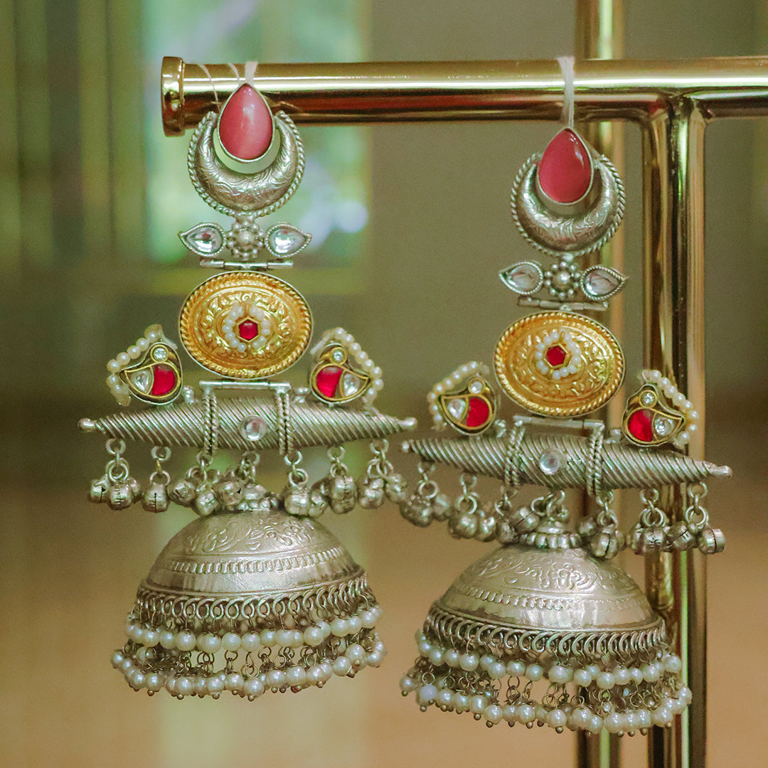 Ornate gold and red earrings with pearl details on a stand.