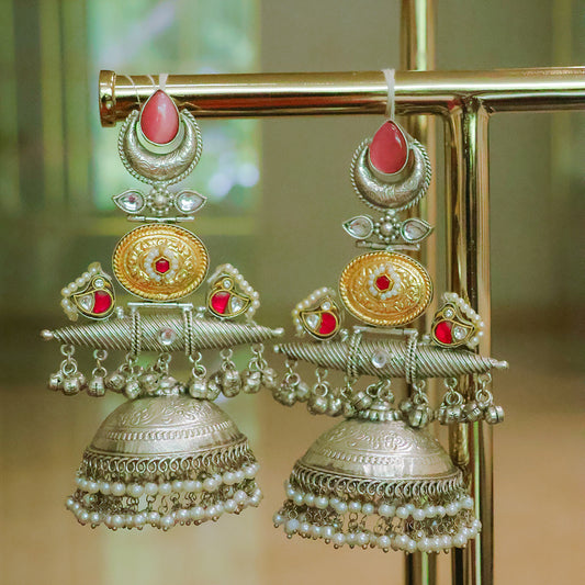 Ornate silver and gold earrings with red stones on a stand.