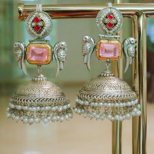 Ornate earrings with pink gemstones and pearl details on a stand.