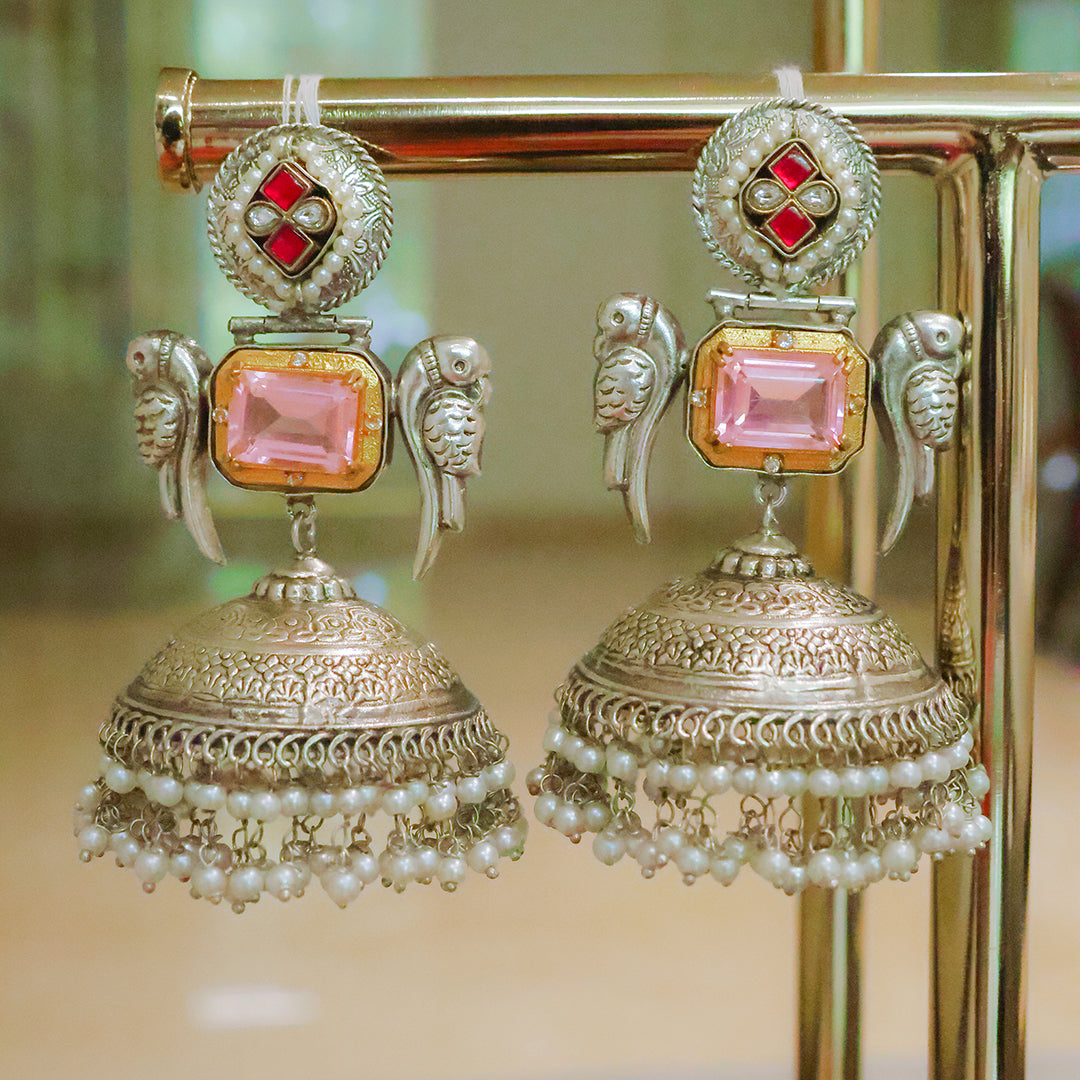 Ornate earrings with pink gemstones and pearl details on a stand.