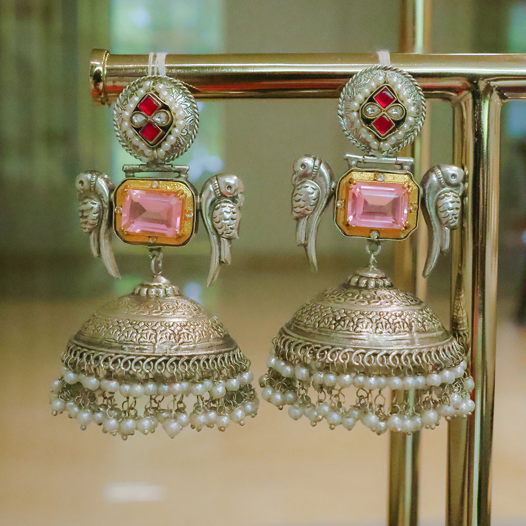 Ornate earrings with pink gemstones and pearl details on a stand.