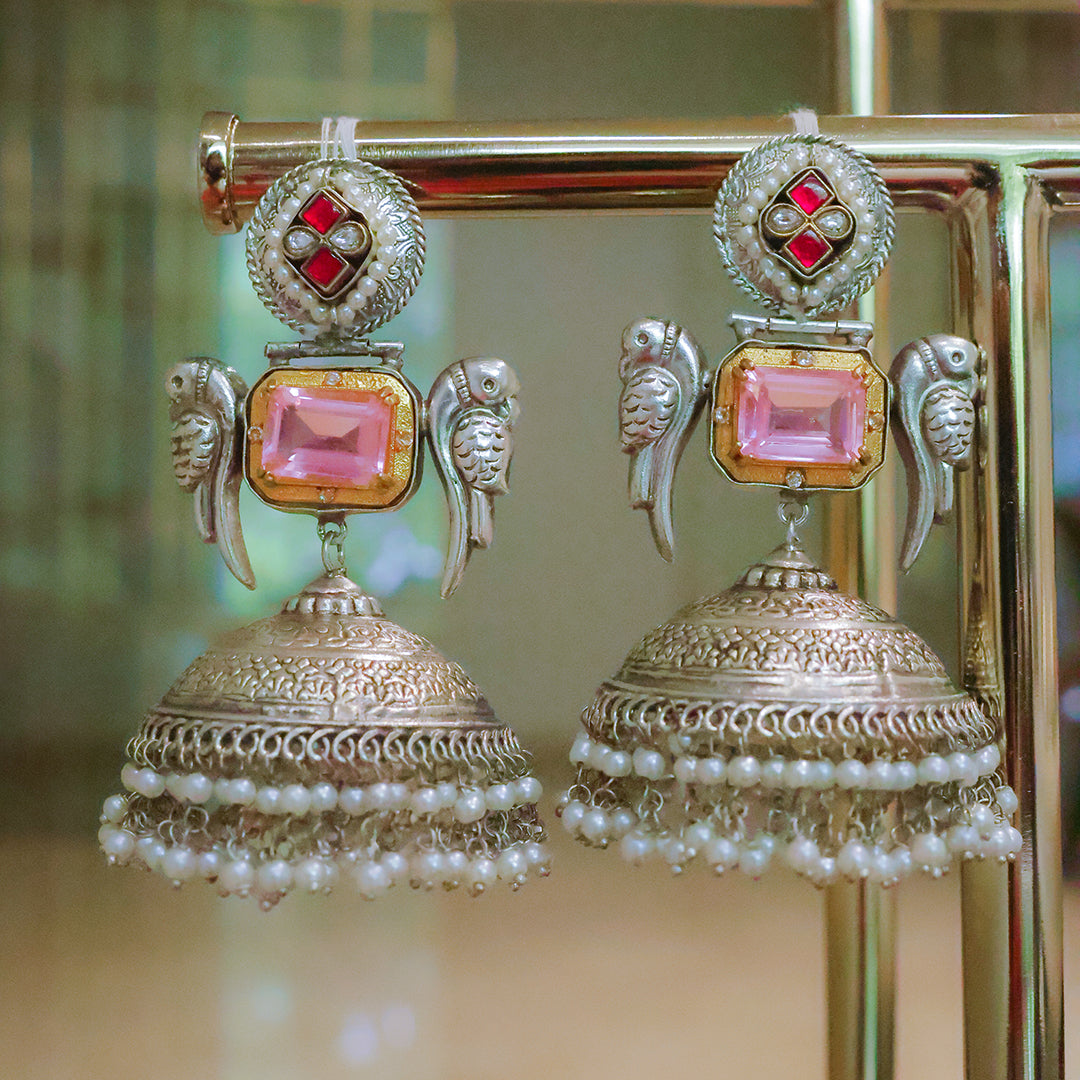 Ornate earrings with pink gemstones and pearl details on a stand.
