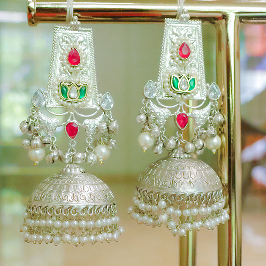 Decorative earrings with pearls and red stones on a reflective surface