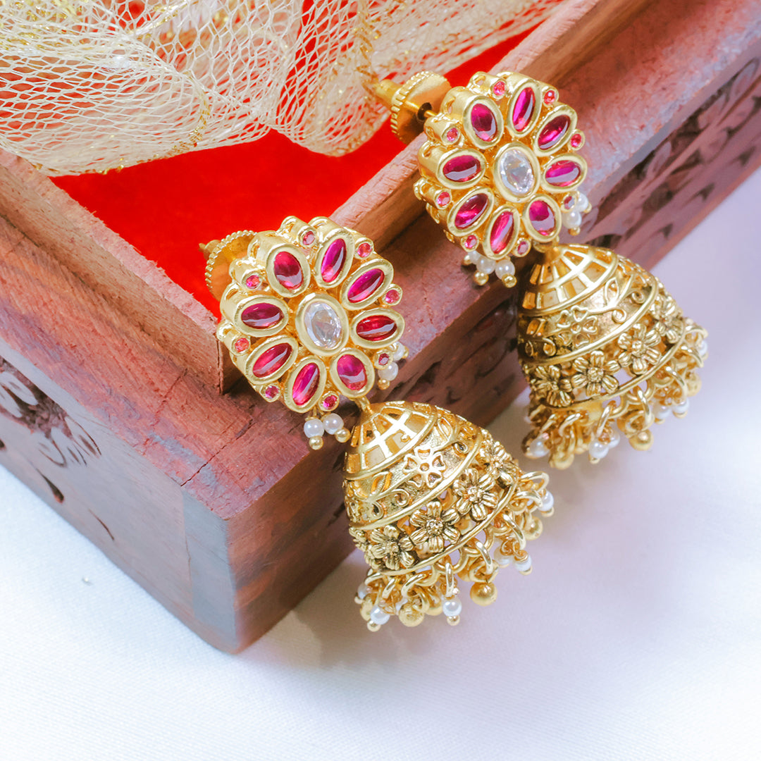 Gold and pink earrings on a wooden surface with a red fabric background