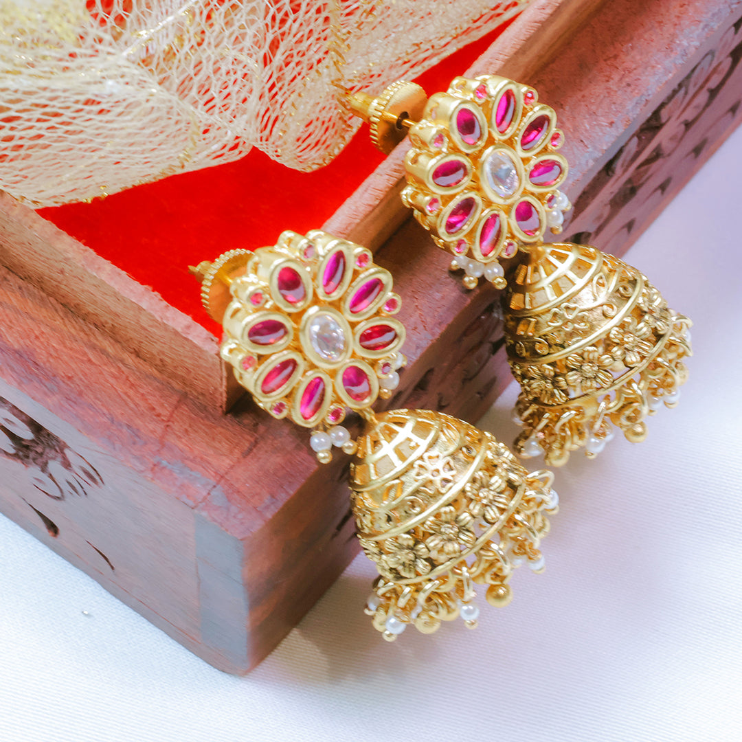 Gold and pink earrings on a wooden box with a red fabric background