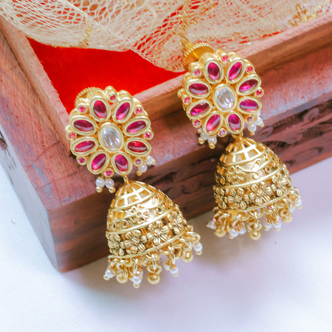 Gold earrings with pink and white stones on a wooden surface