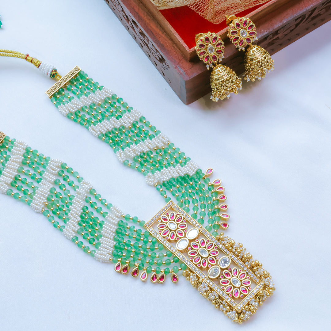 Green beaded necklace with gold and pink floral designs on a white background