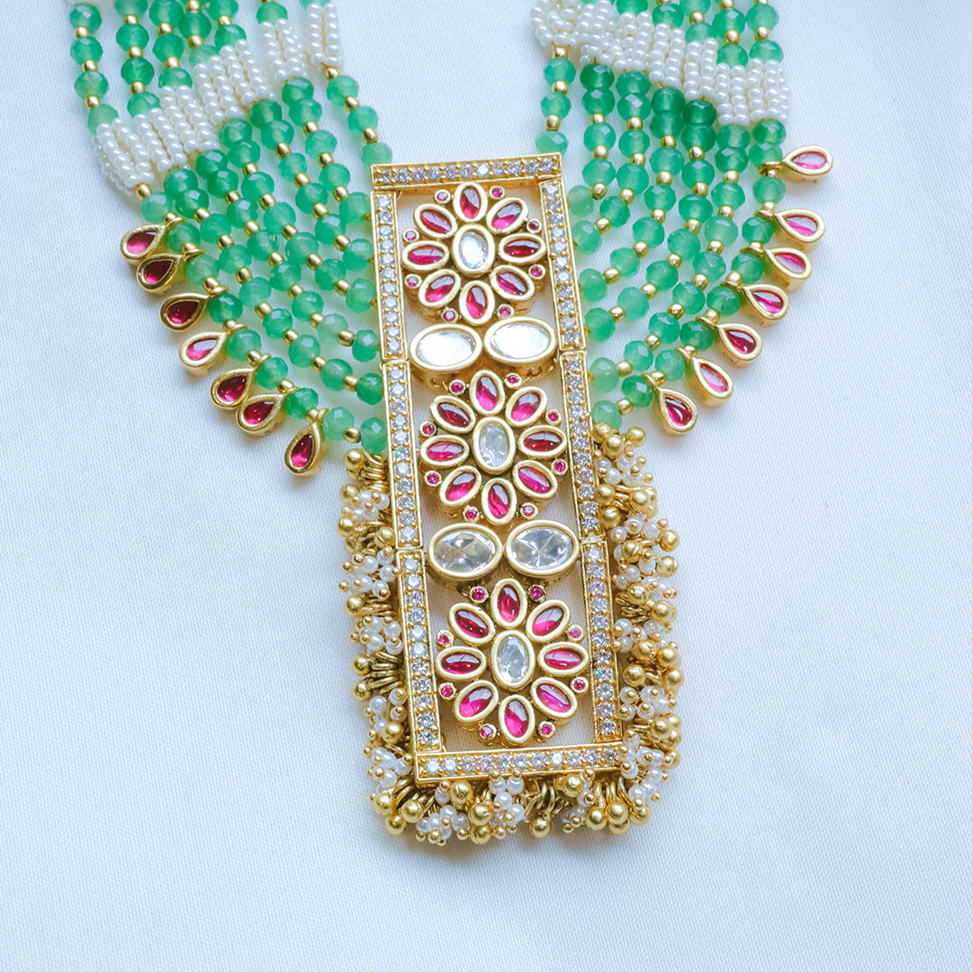 Ornate gold necklace with green beads and pink stones on a white background