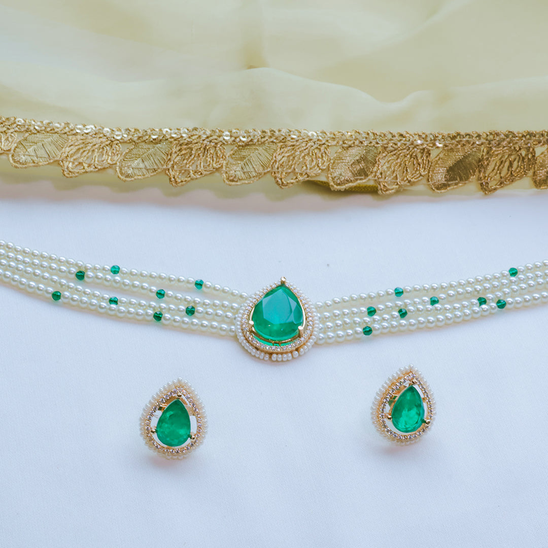 Jewelry set with green gemstones and pearl necklace on a white background