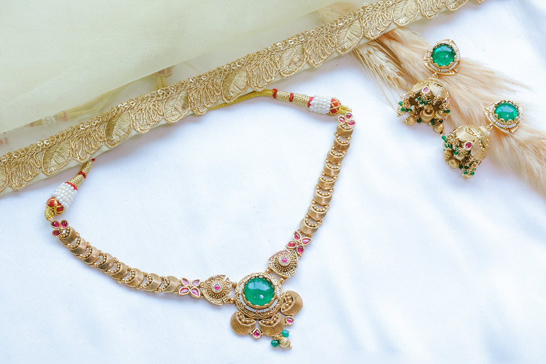 Gold necklace with green gemstones and matching earrings on a white background