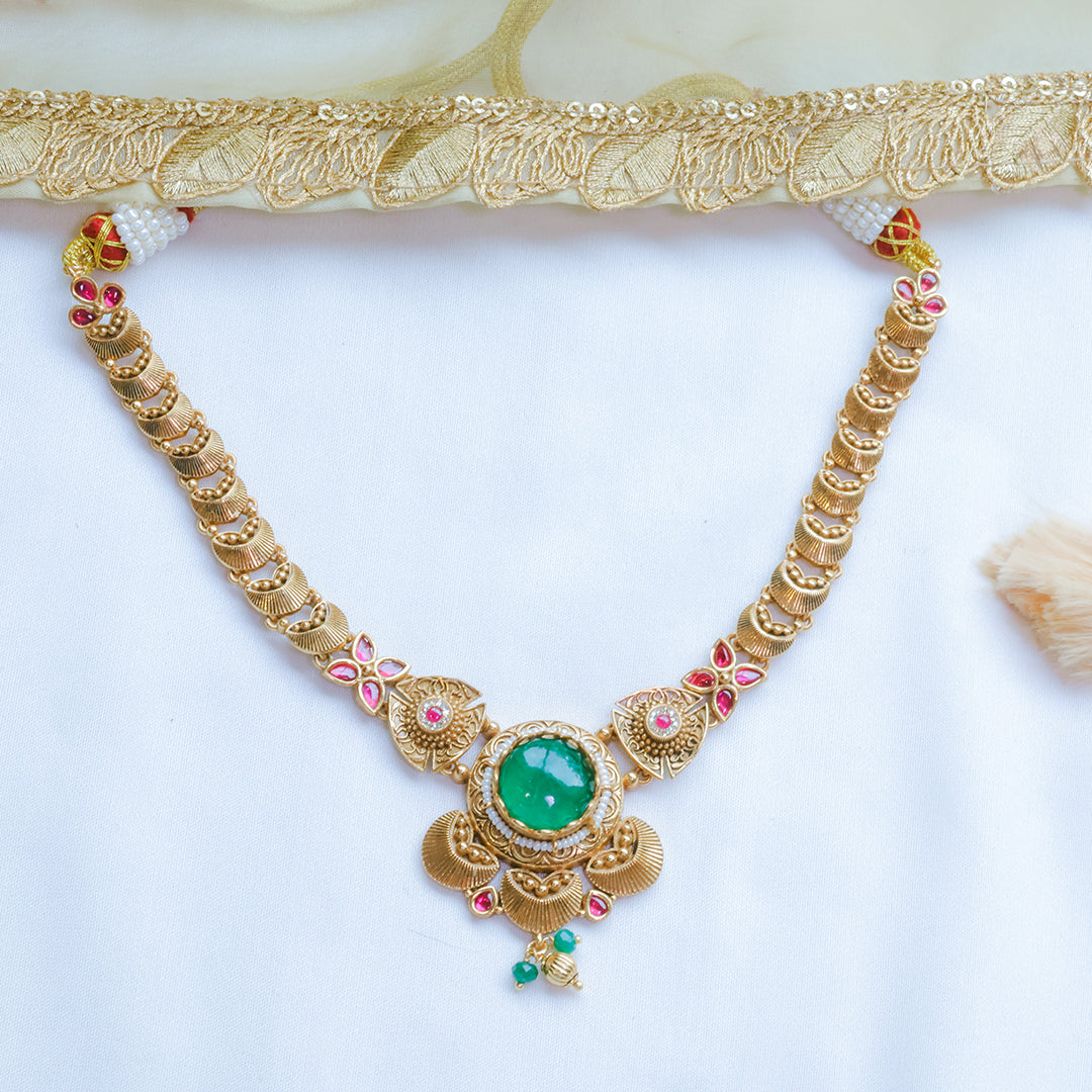 Gold necklace with green gemstone and red stones on a white background