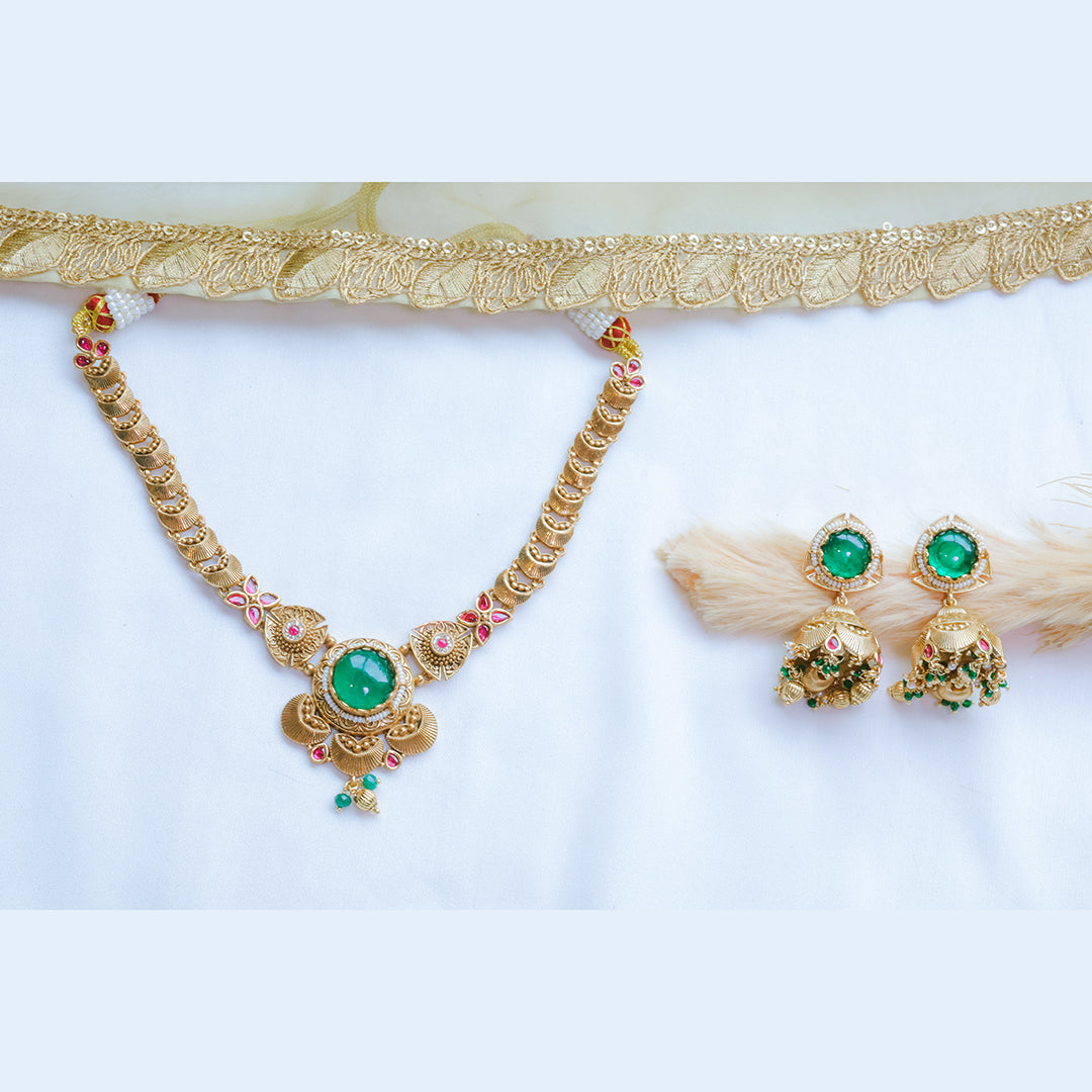 Gold necklace with green gemstones and matching earrings on a white background