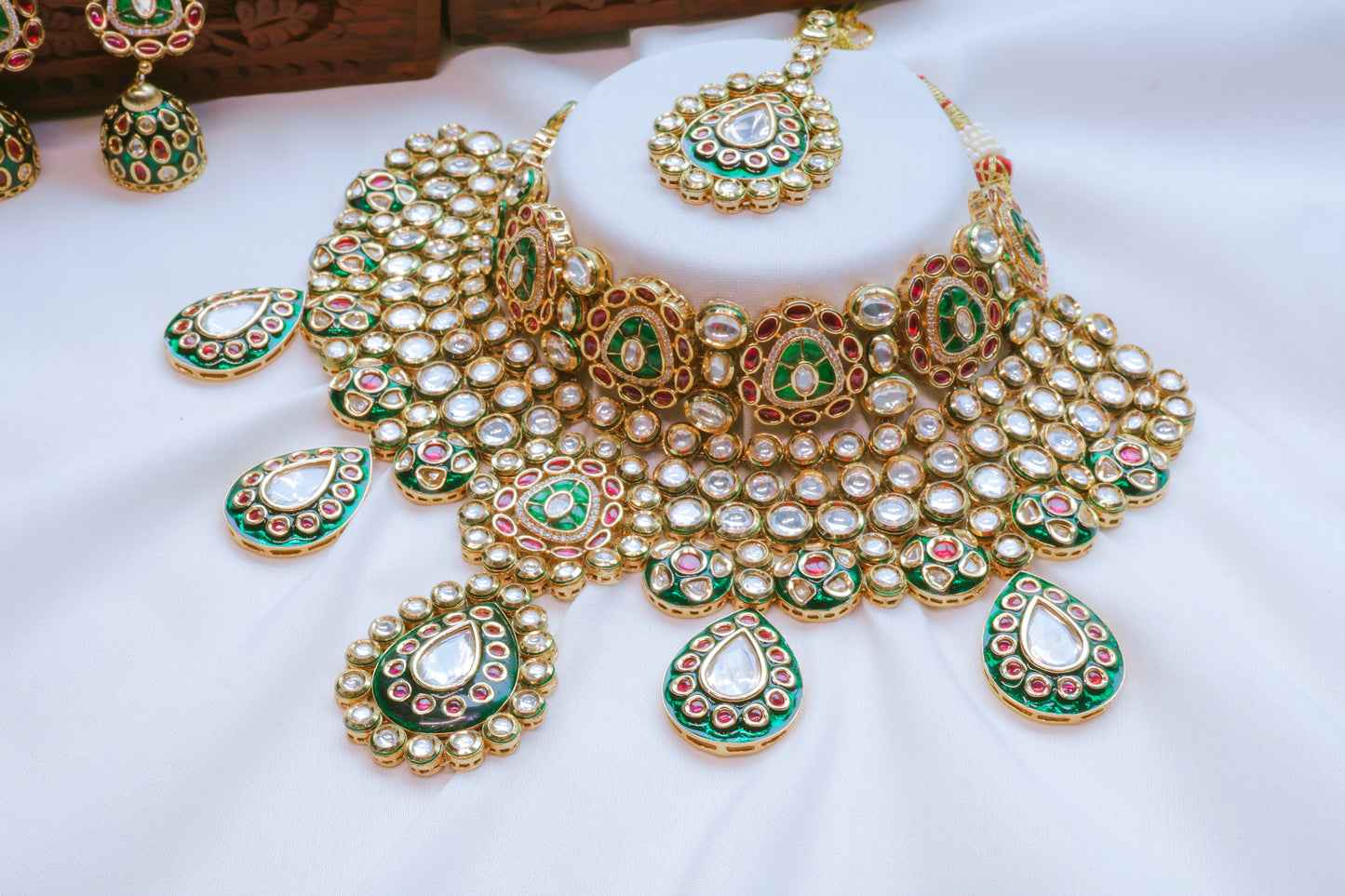 Ornate gold necklace with green and red accents on a white background