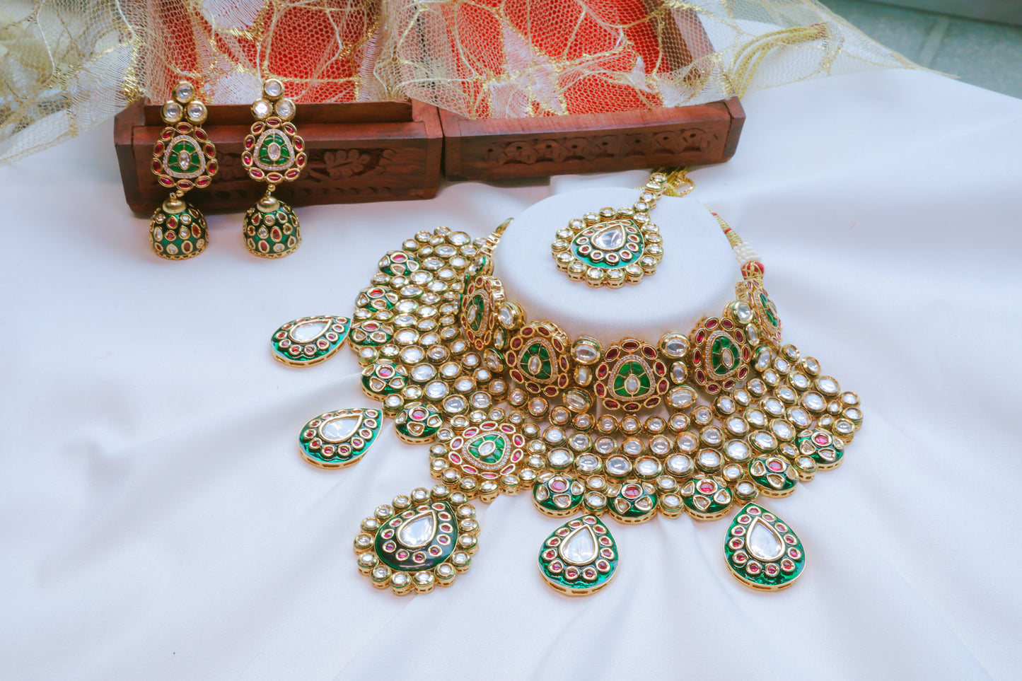 Ornate gold and green jewelry set with matching earrings on a white fabric background.