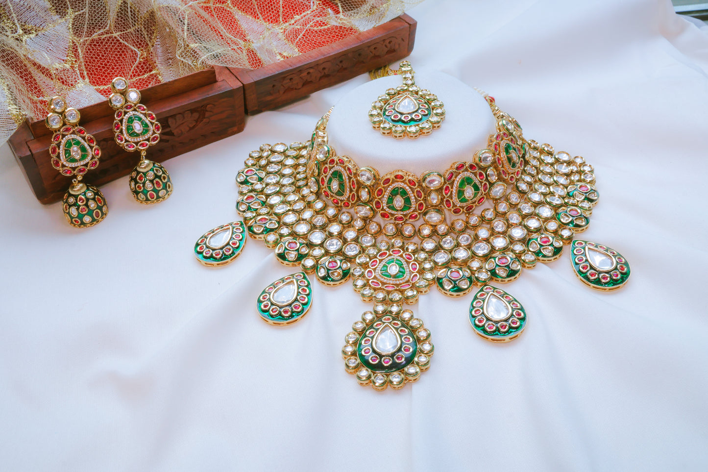 Gold necklace with green and red stones on a white surface