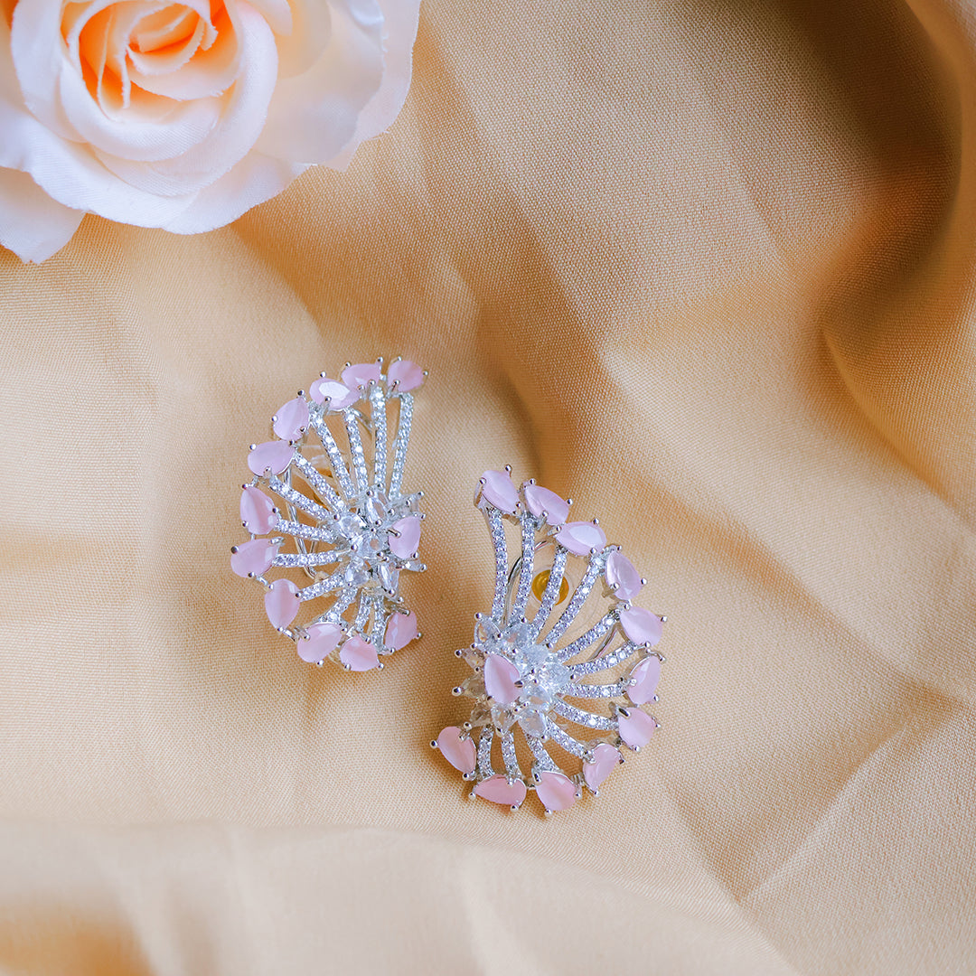 Pair of pink and silver earrings on a beige fabric background with a white rose.