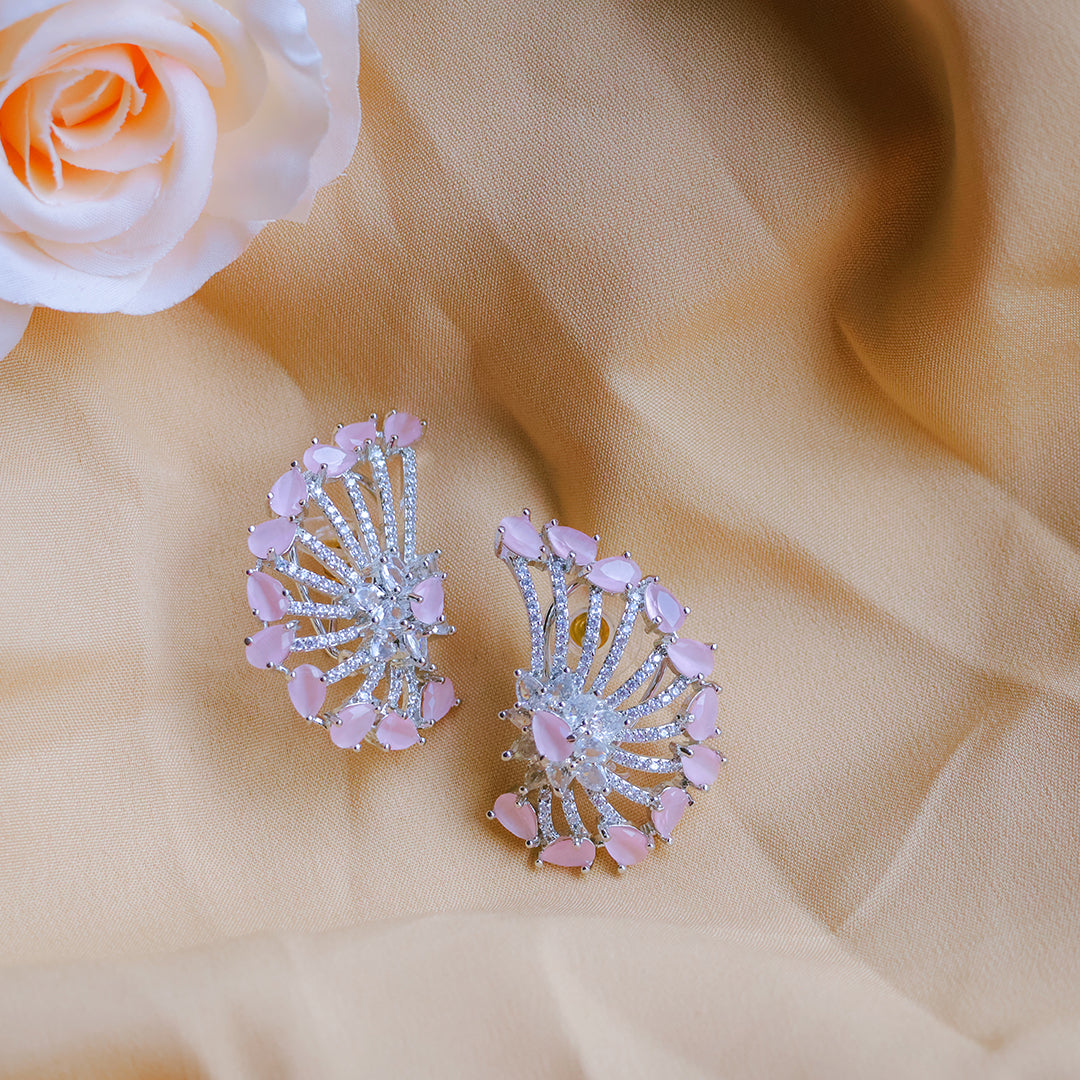 Pair of pink and silver earrings on a beige fabric background with a rose.