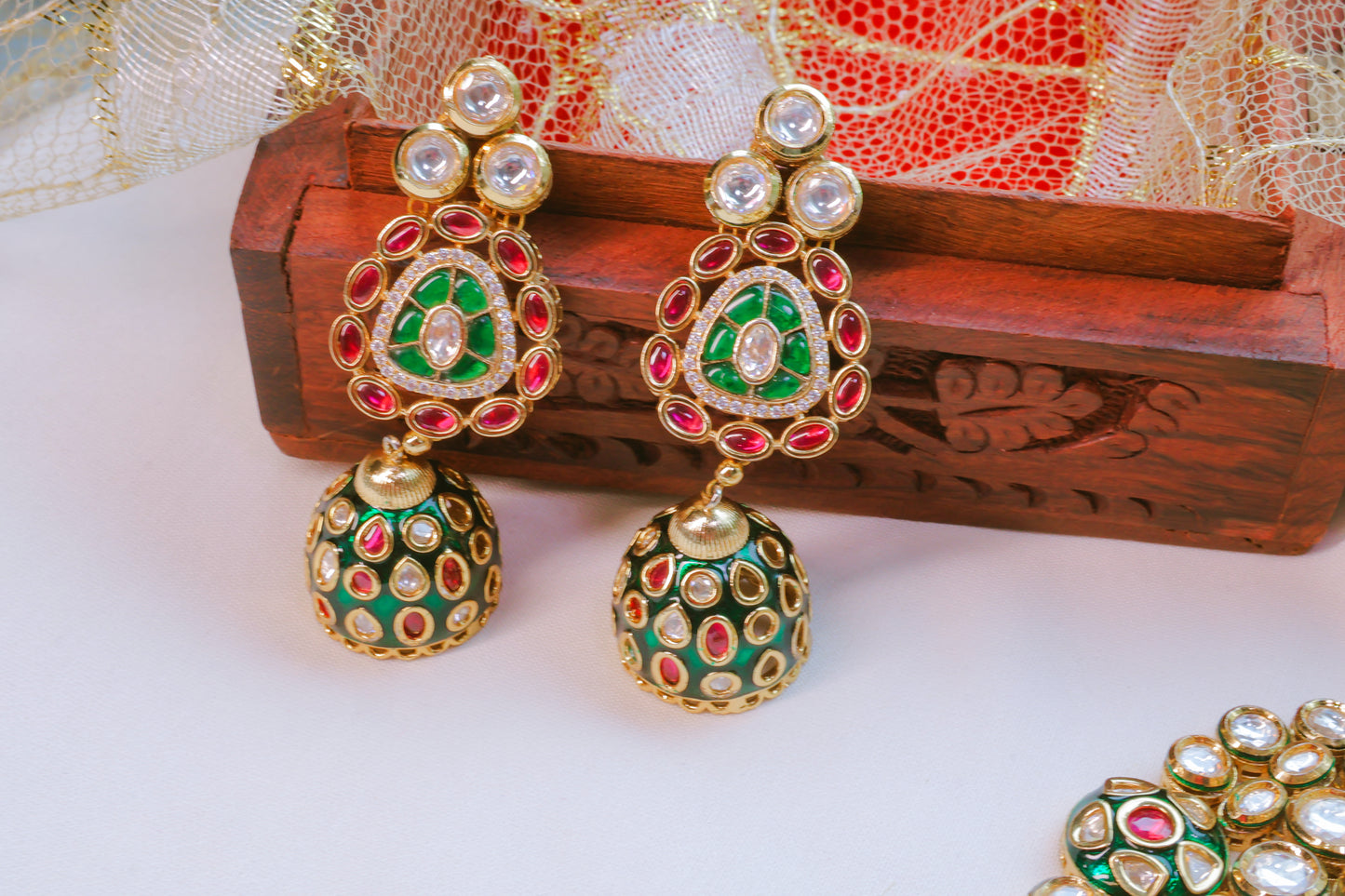 Ornate earrings with green, red, and gold colors on a white surface.