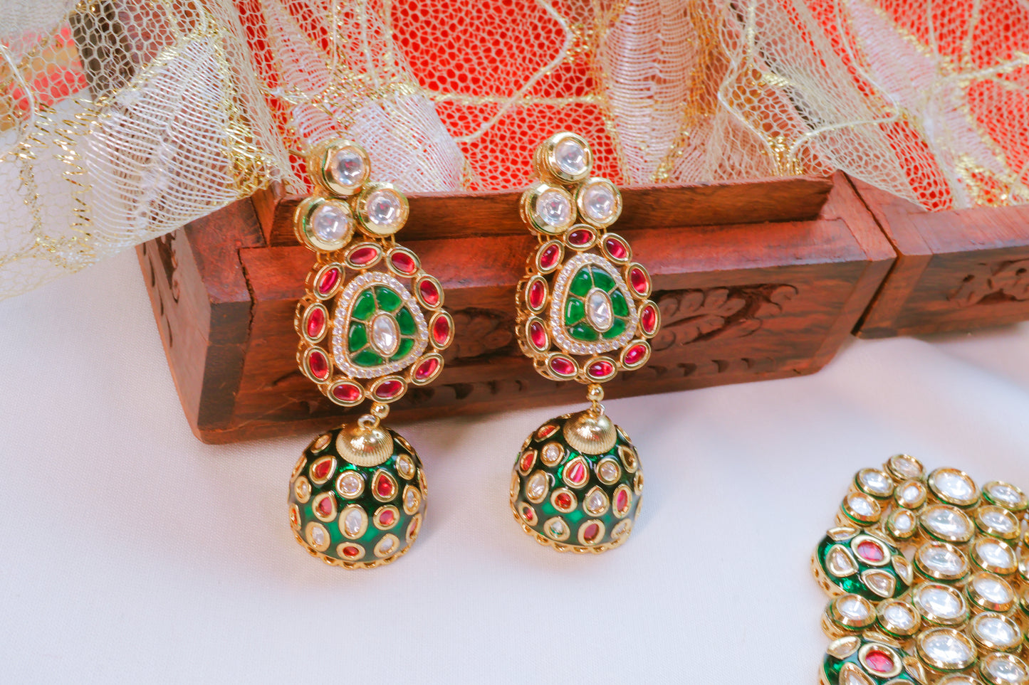 Ornate earrings with green and red accents on a wooden box