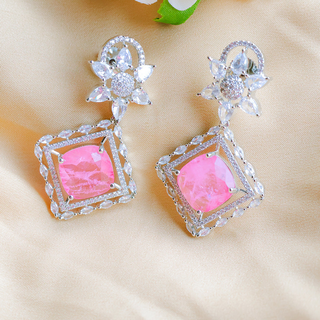 Pair of earrings with pink gemstones and diamond-like accents on a beige background