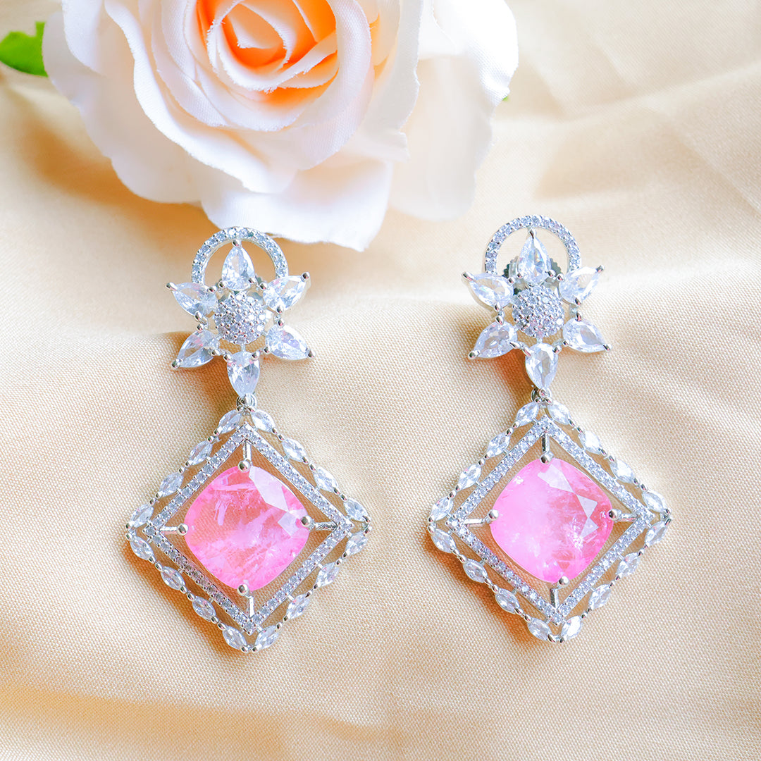 Pair of earrings with pink gemstones and silver accents on a beige fabric background.
