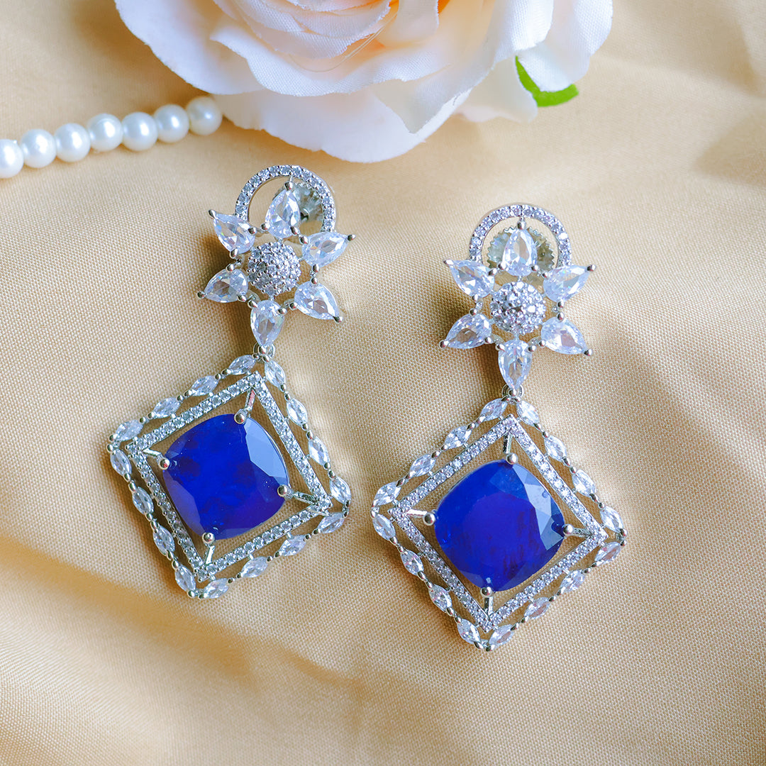 Pair of blue gemstone earrings with silver detailing on a beige fabric background.