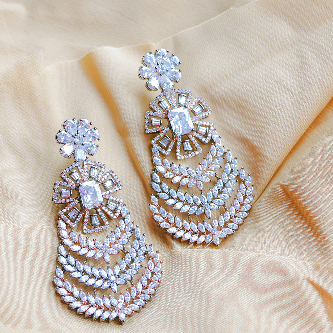 Pair of ornate earrings with clear gemstones on a beige fabric background