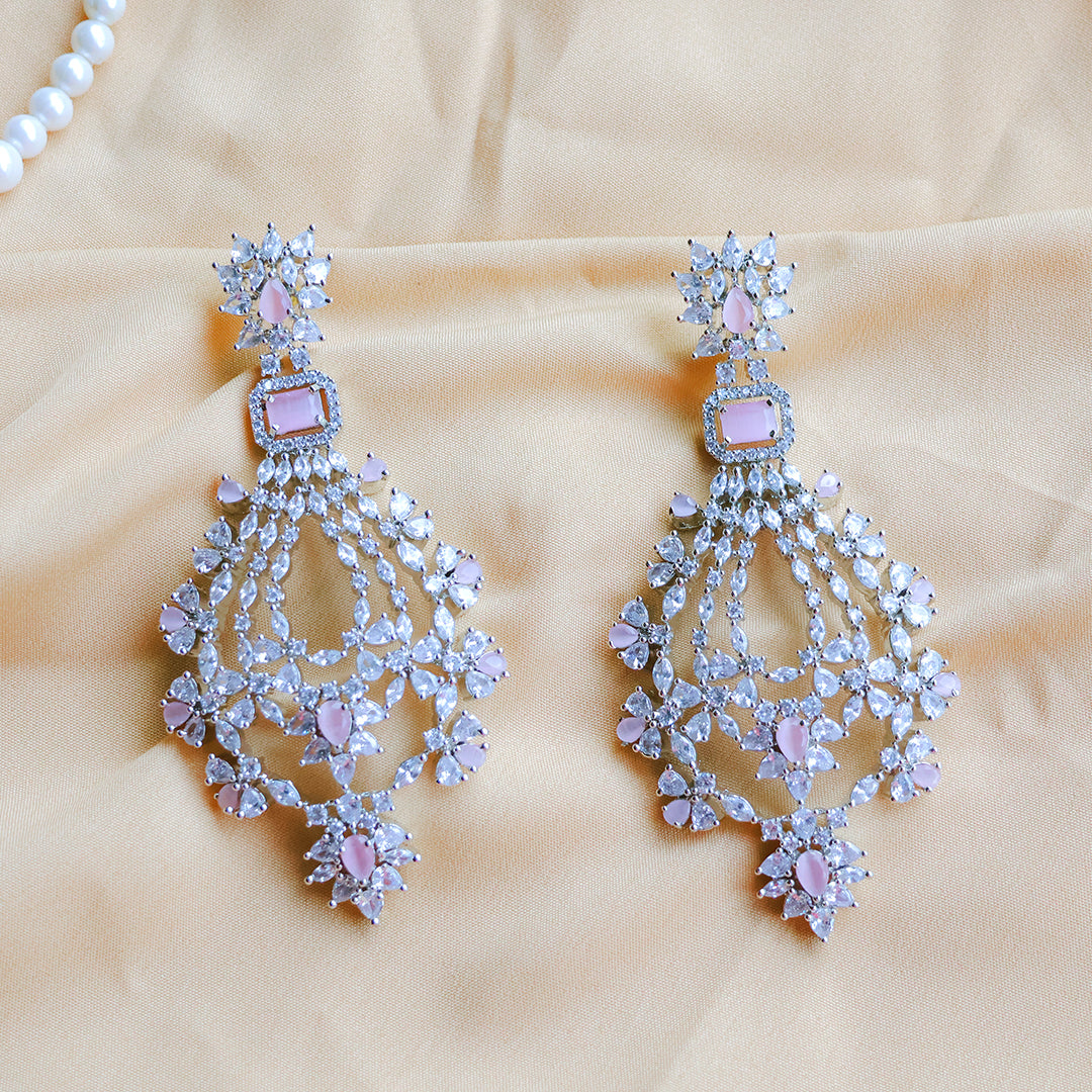 Pair of chandelier earrings with pink gemstones on a beige fabric background