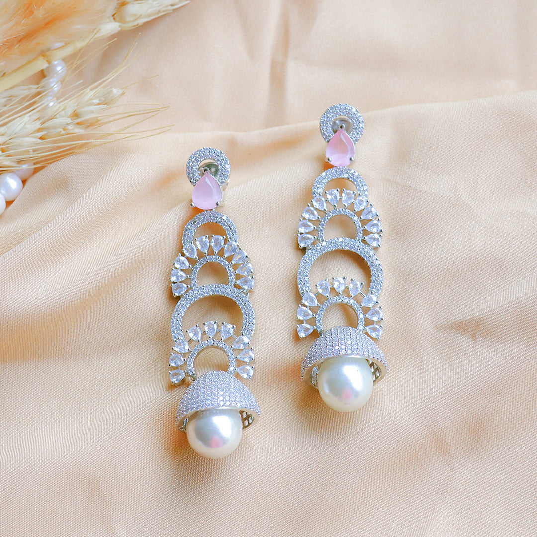 Pair of silver earrings with pearls and pink stones on a beige fabric background