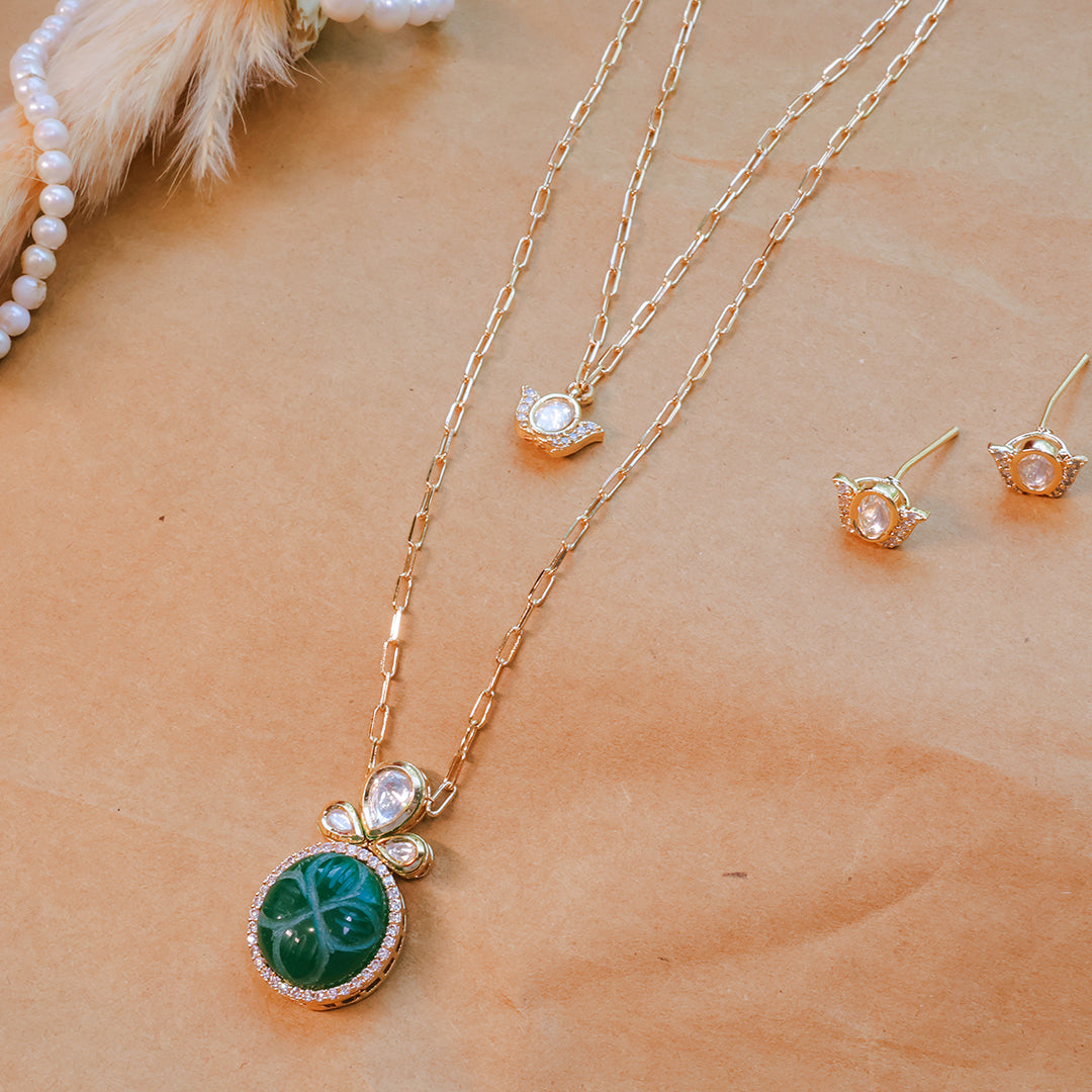 Gold necklace with green pendant and matching earrings on a person's neck and chest.