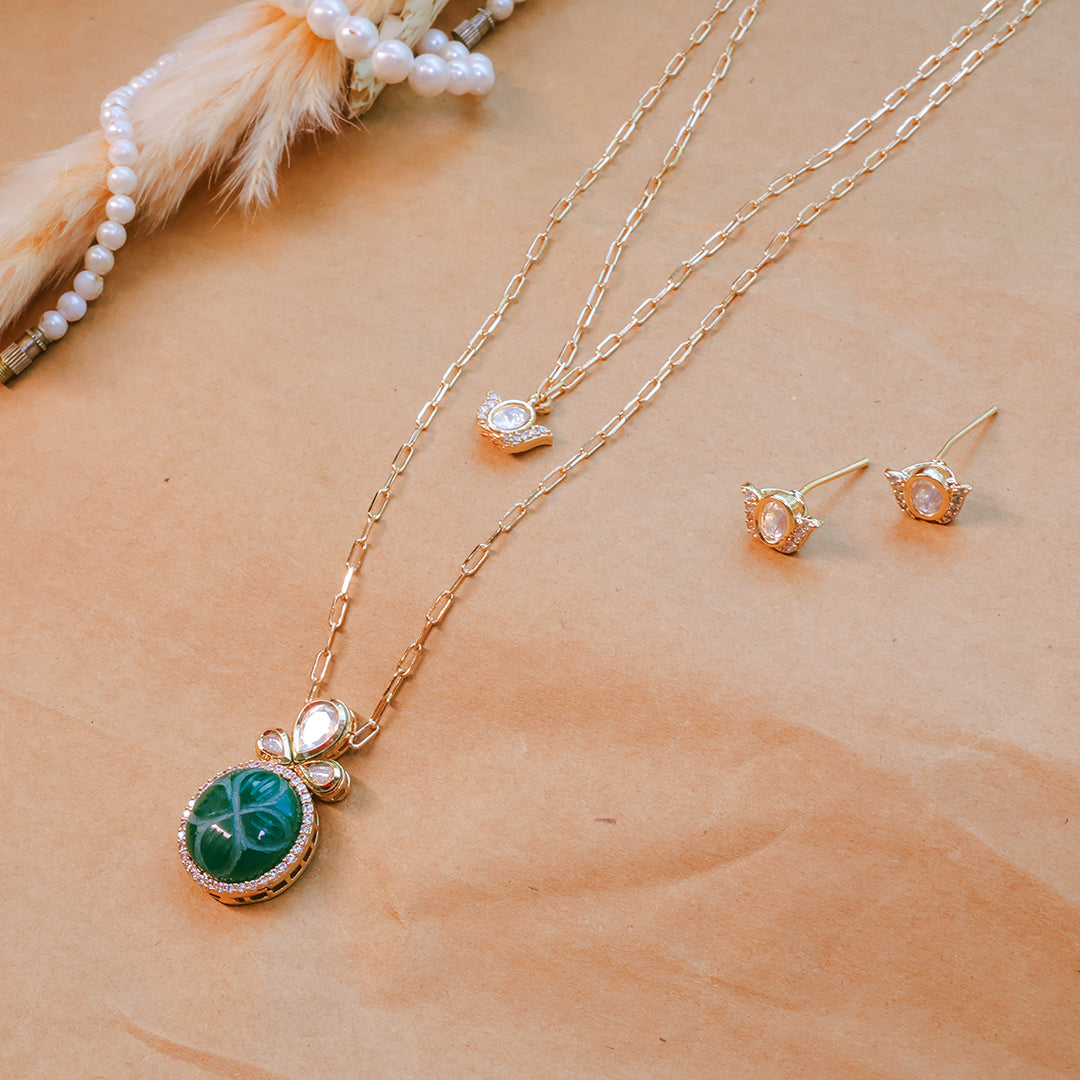 Gold necklace with green pendant and matching earrings on a beige surface