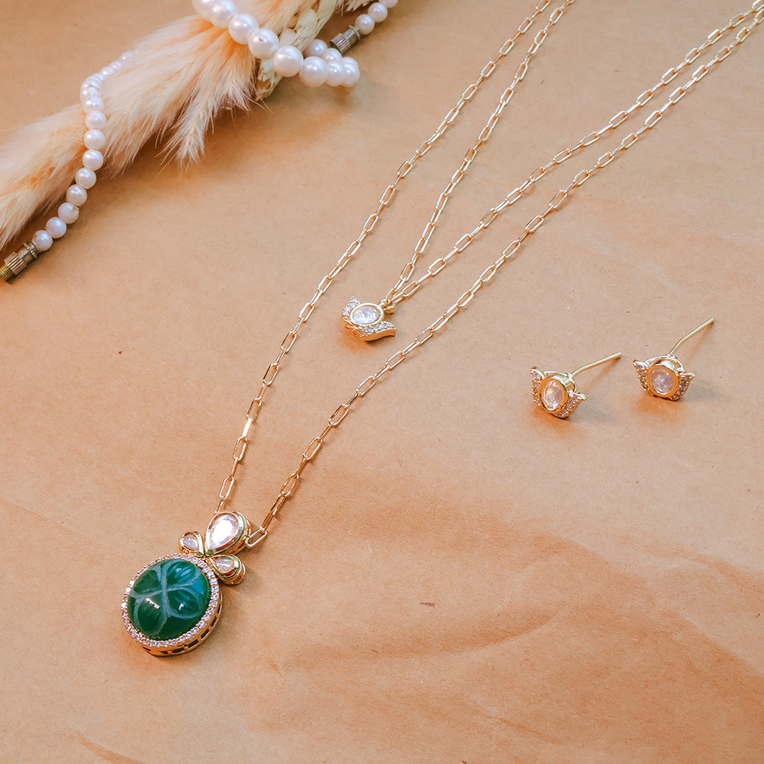 Gold necklace with green pendant and matching earrings on a beige surface.