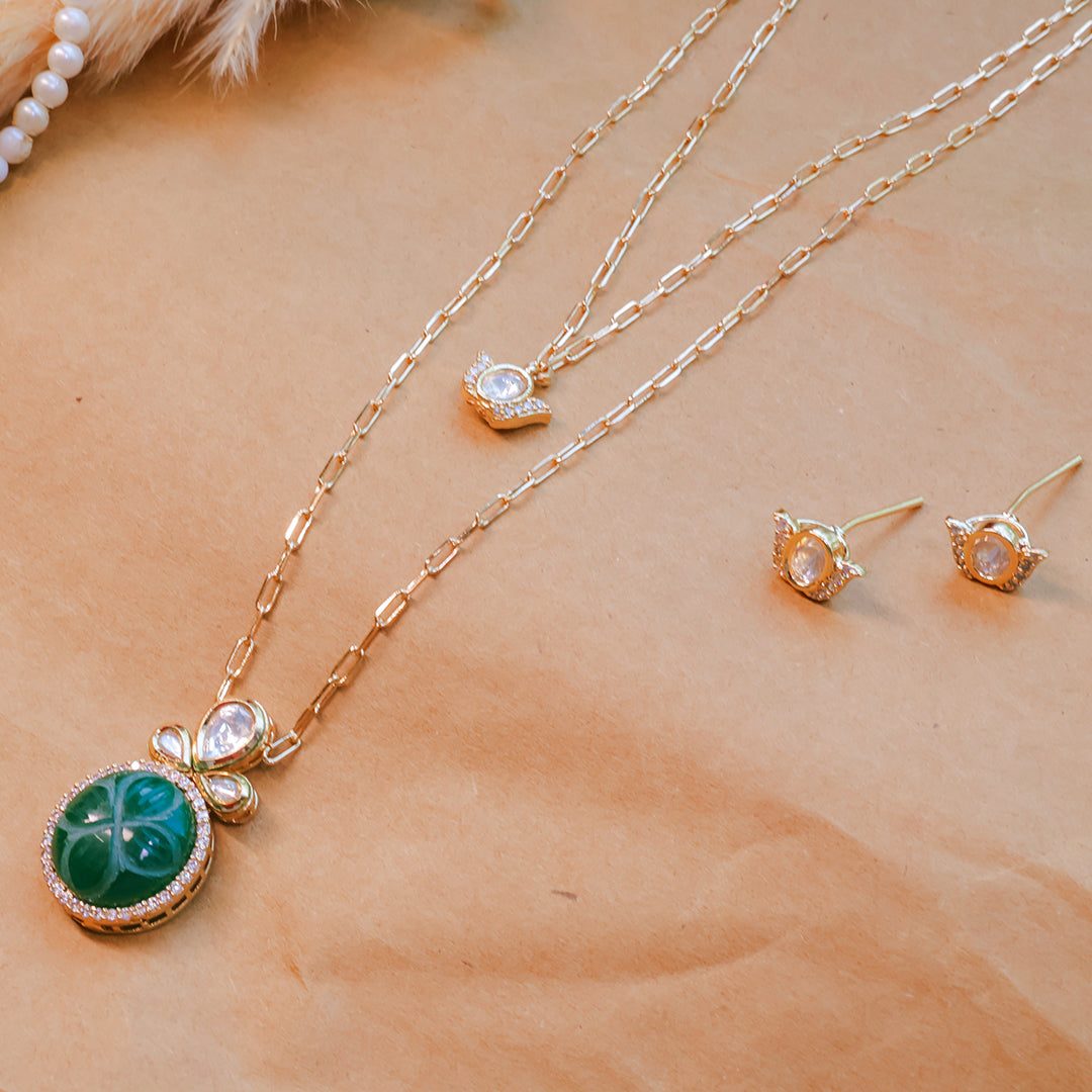 Gold necklace with green pendant and matching earrings on a beige surface