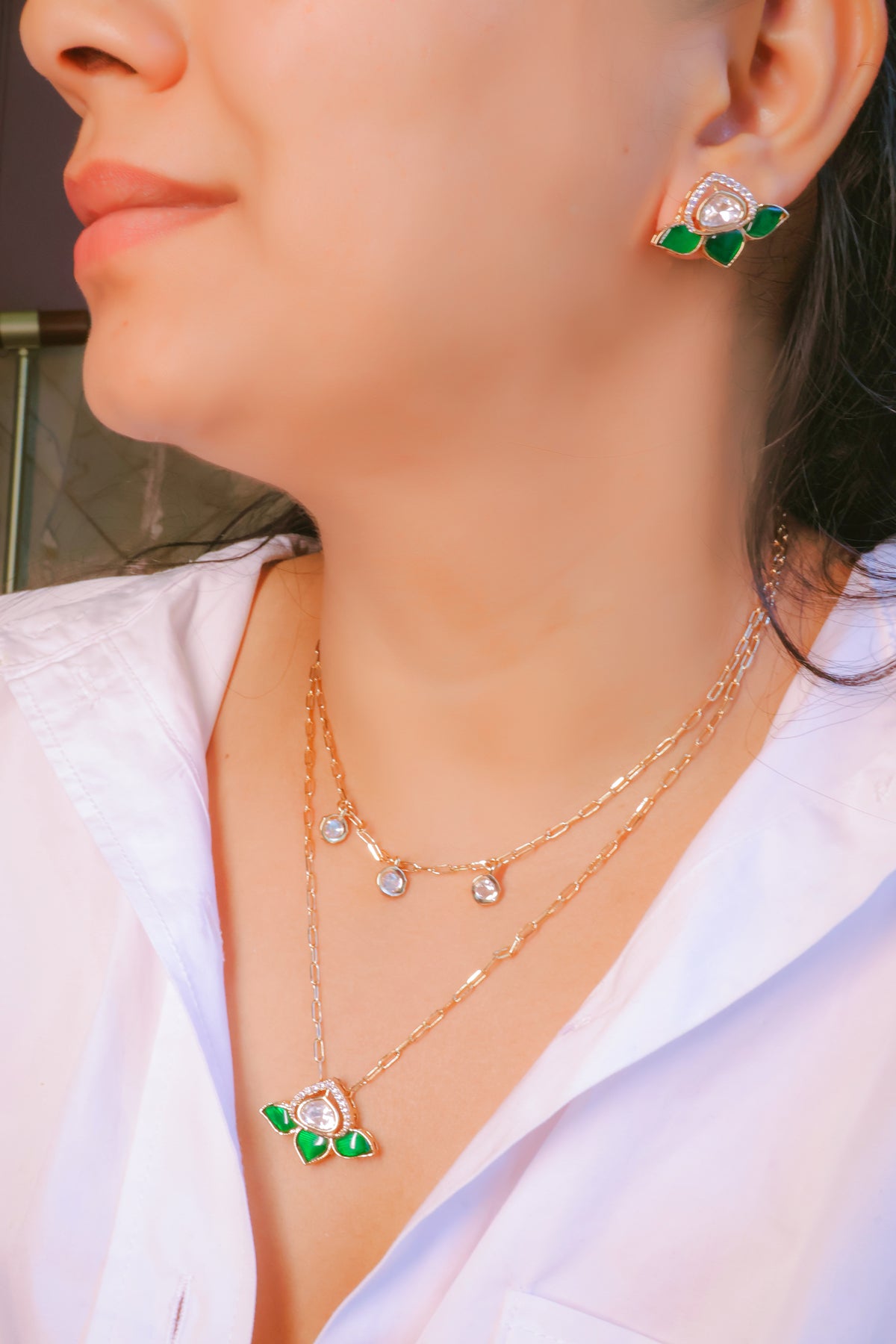 Close-up of a person wearing gold necklaces and earrings with green accents.