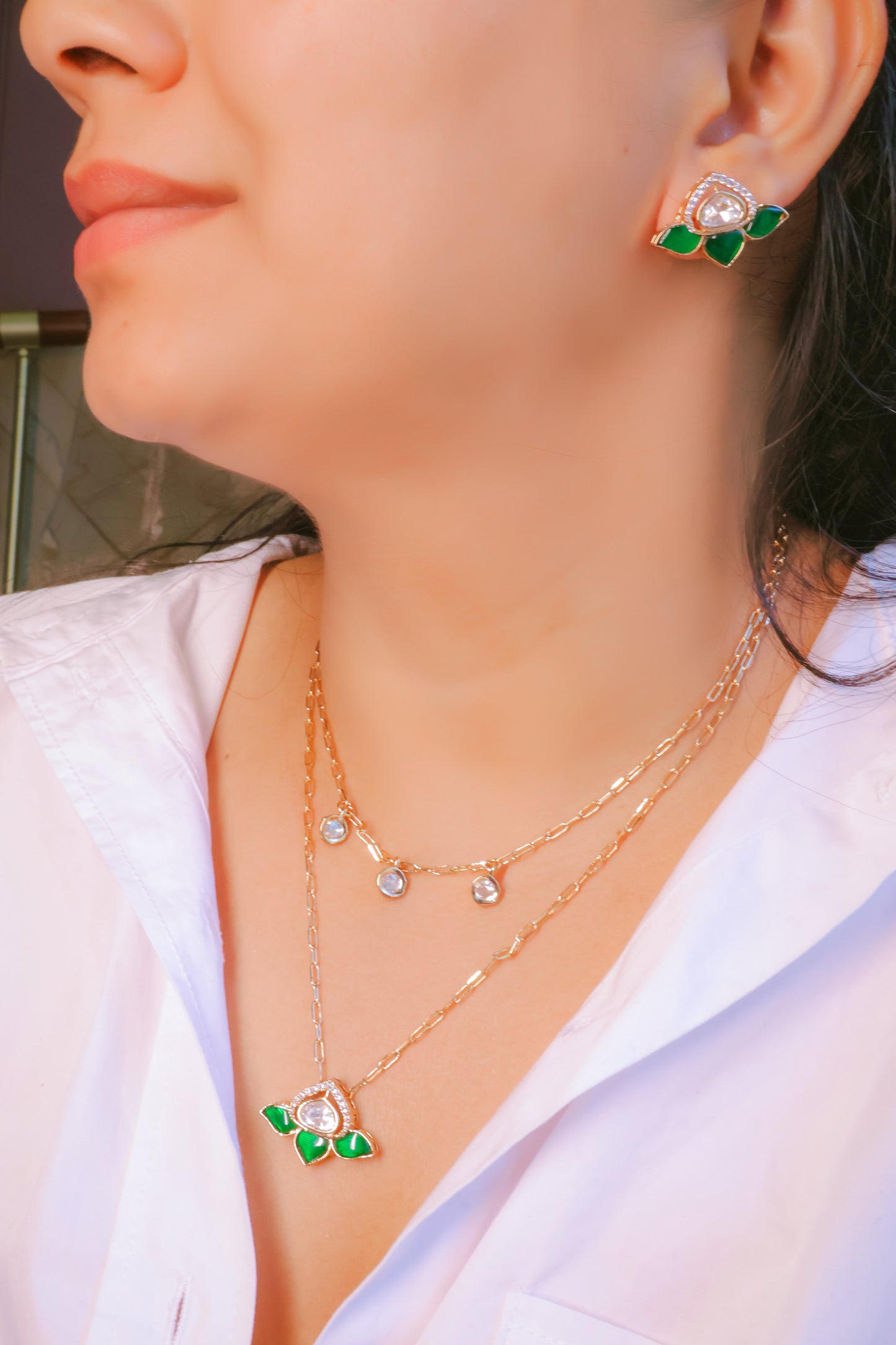 Close-up of a person wearing gold necklaces and earrings with green accents.
