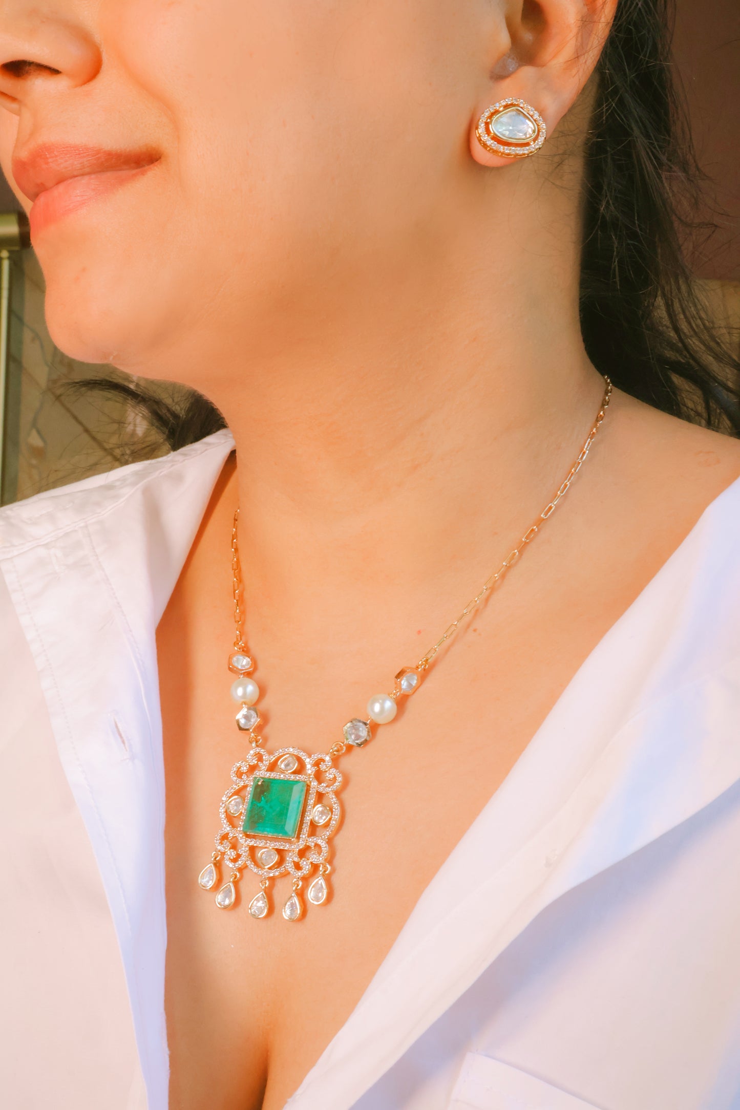 Close-up of a person wearing a gold necklace with a green gemstone and matching earrings.