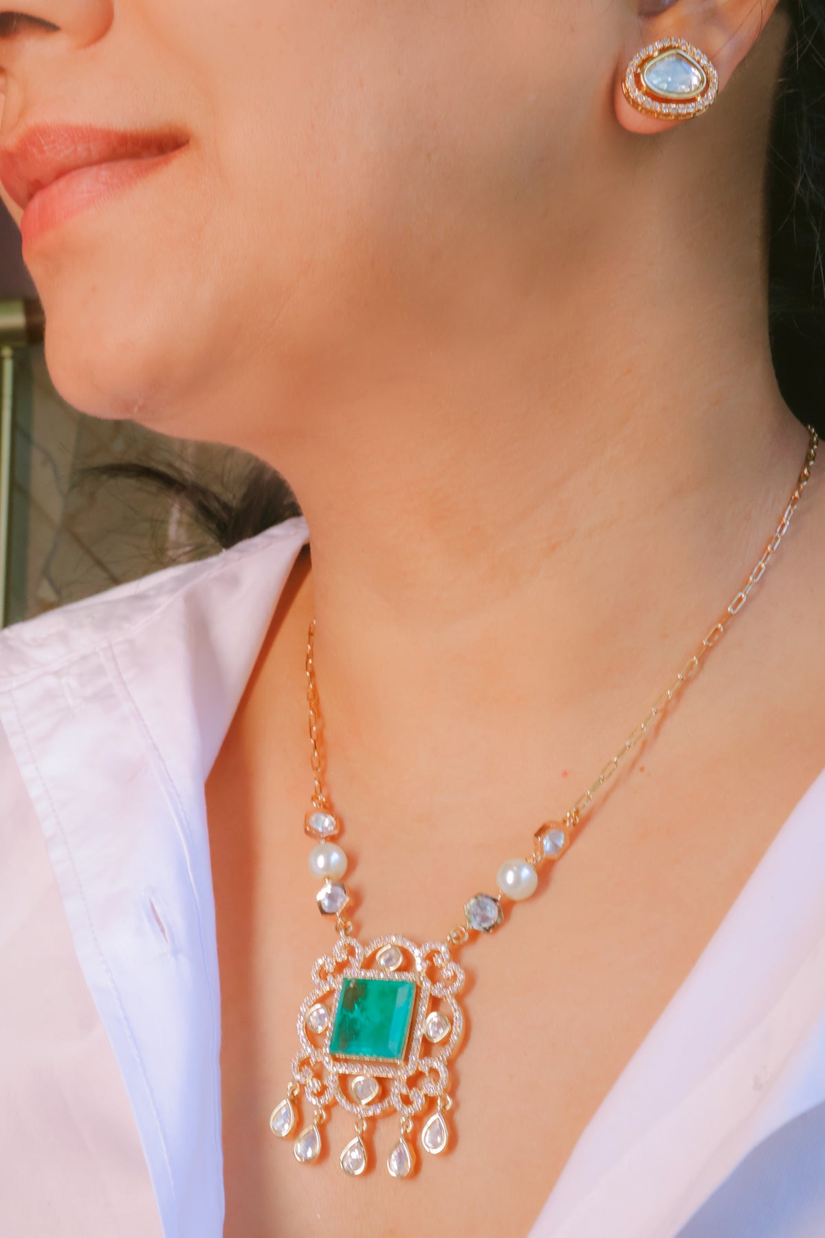 Close-up of a person wearing a gold necklace with a green gemstone and pearl accents.