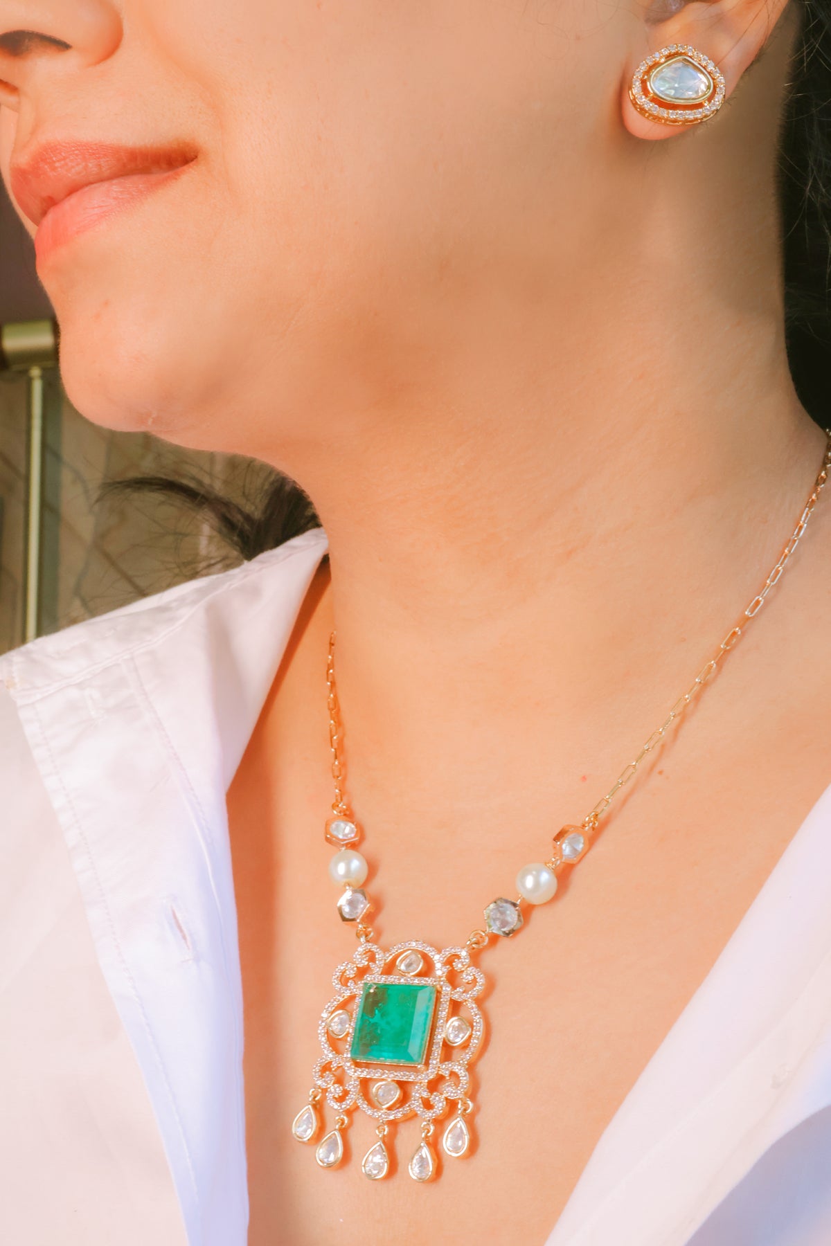 Close-up of a person wearing a gold necklace with a green gemstone and matching earrings.