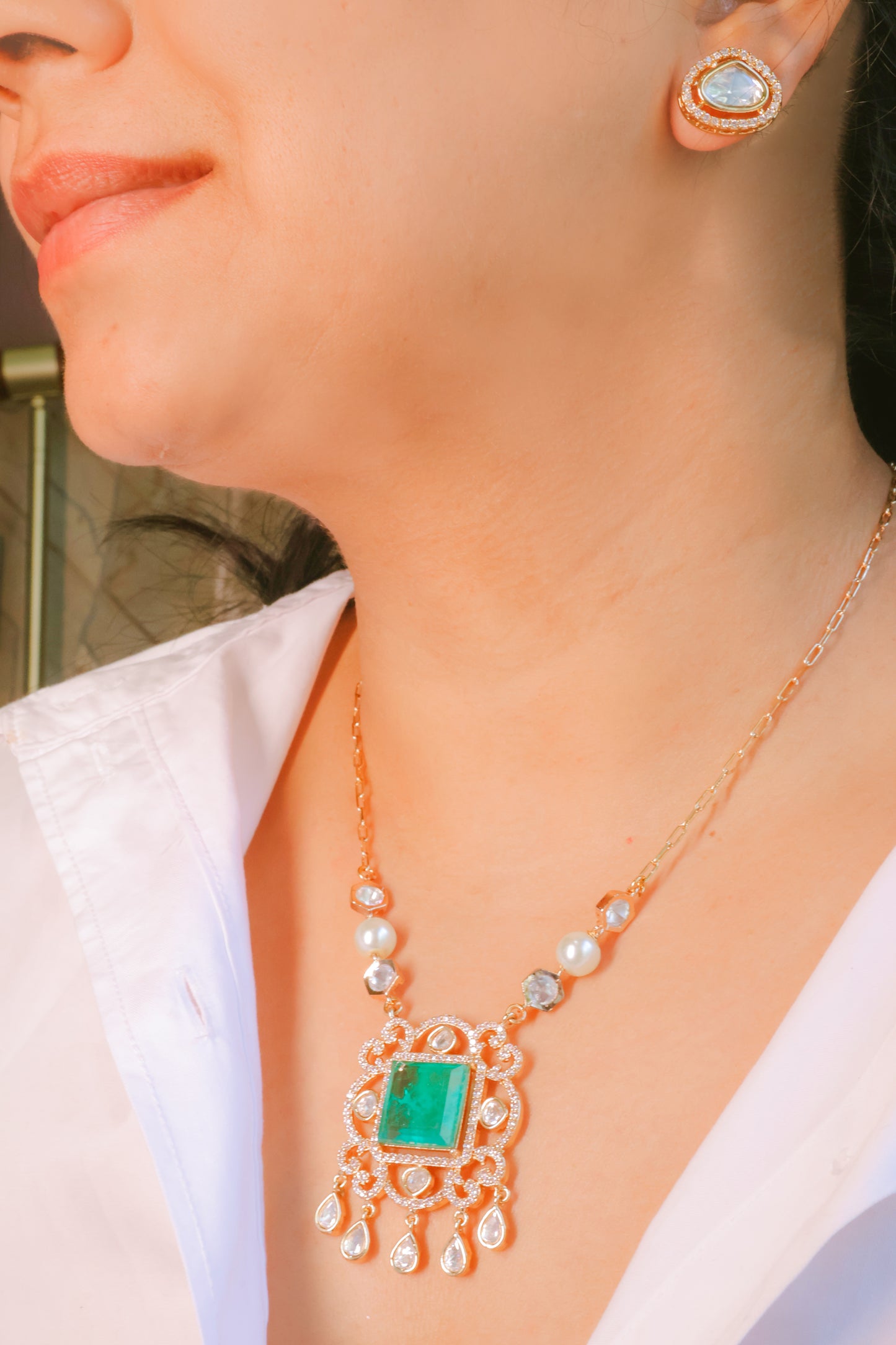 Close-up of a person wearing a gold necklace with a green gemstone and matching earrings.