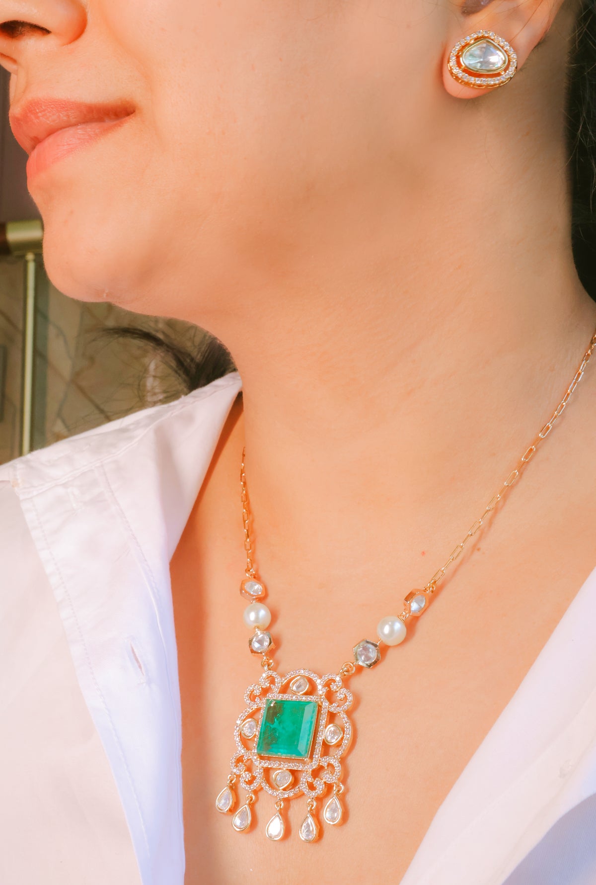 Close-up of a person wearing a gold necklace with a green gemstone pendant and matching earrings.