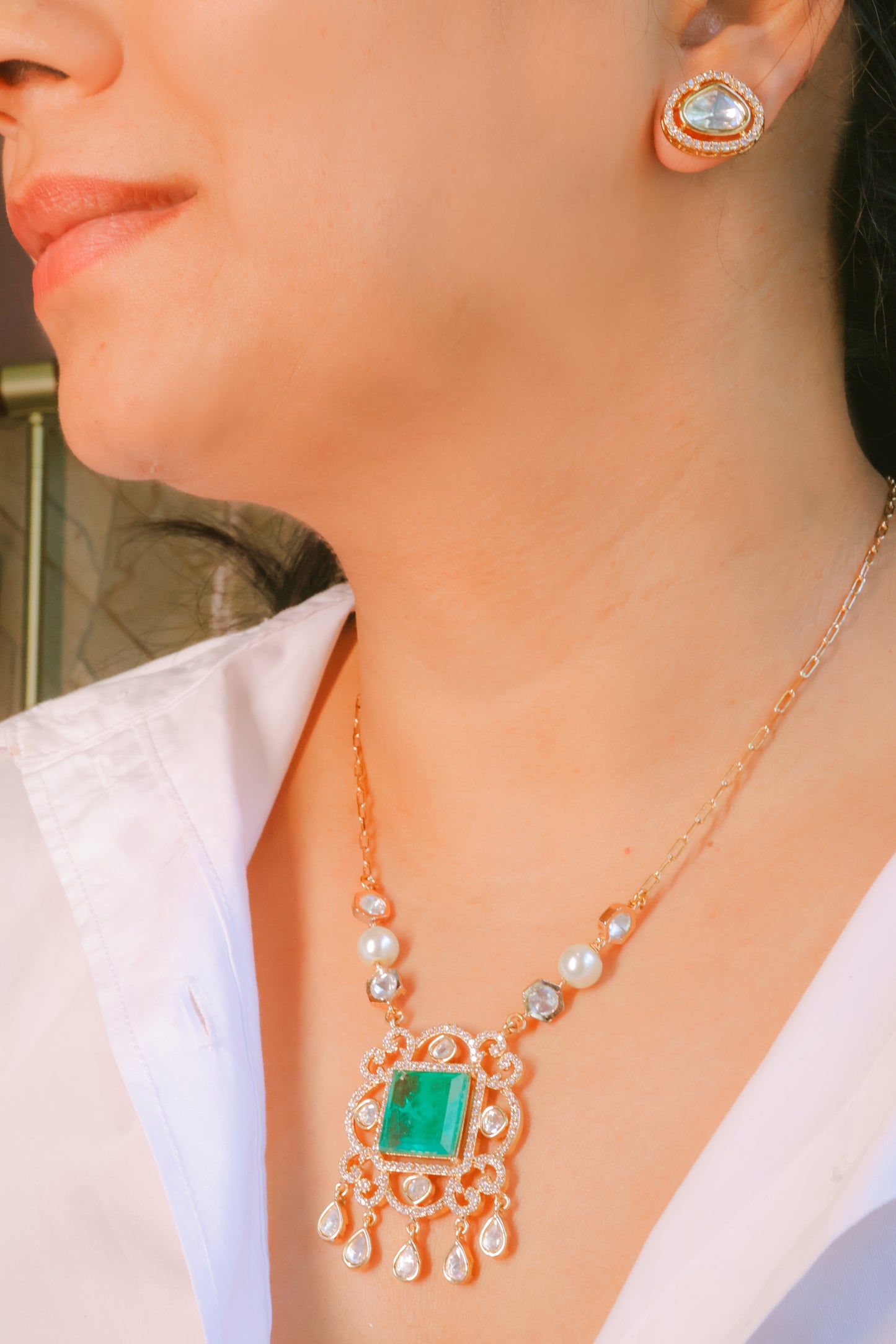 Close-up of a person wearing a gold necklace with a green gemstone and matching earrings.