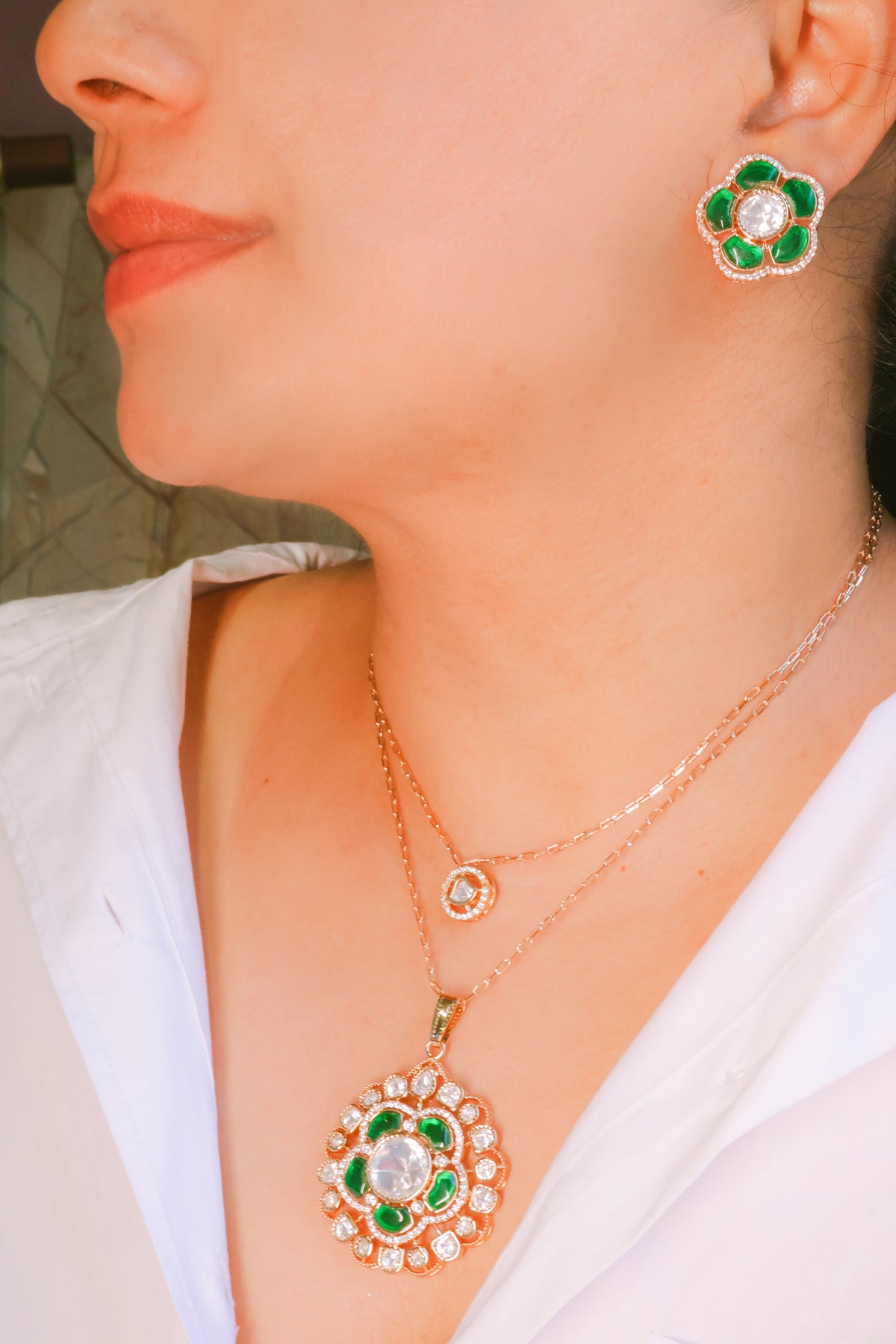 Close-up of a person wearing a necklace and earrings with green and red stones.