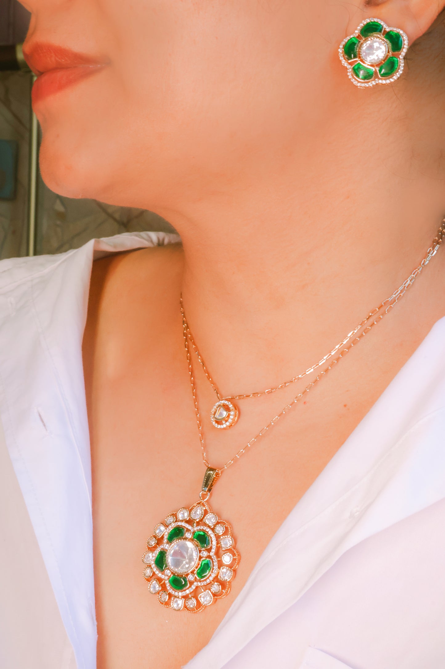 Close-up of a person wearing a gold necklace and earrings with green and red accents.