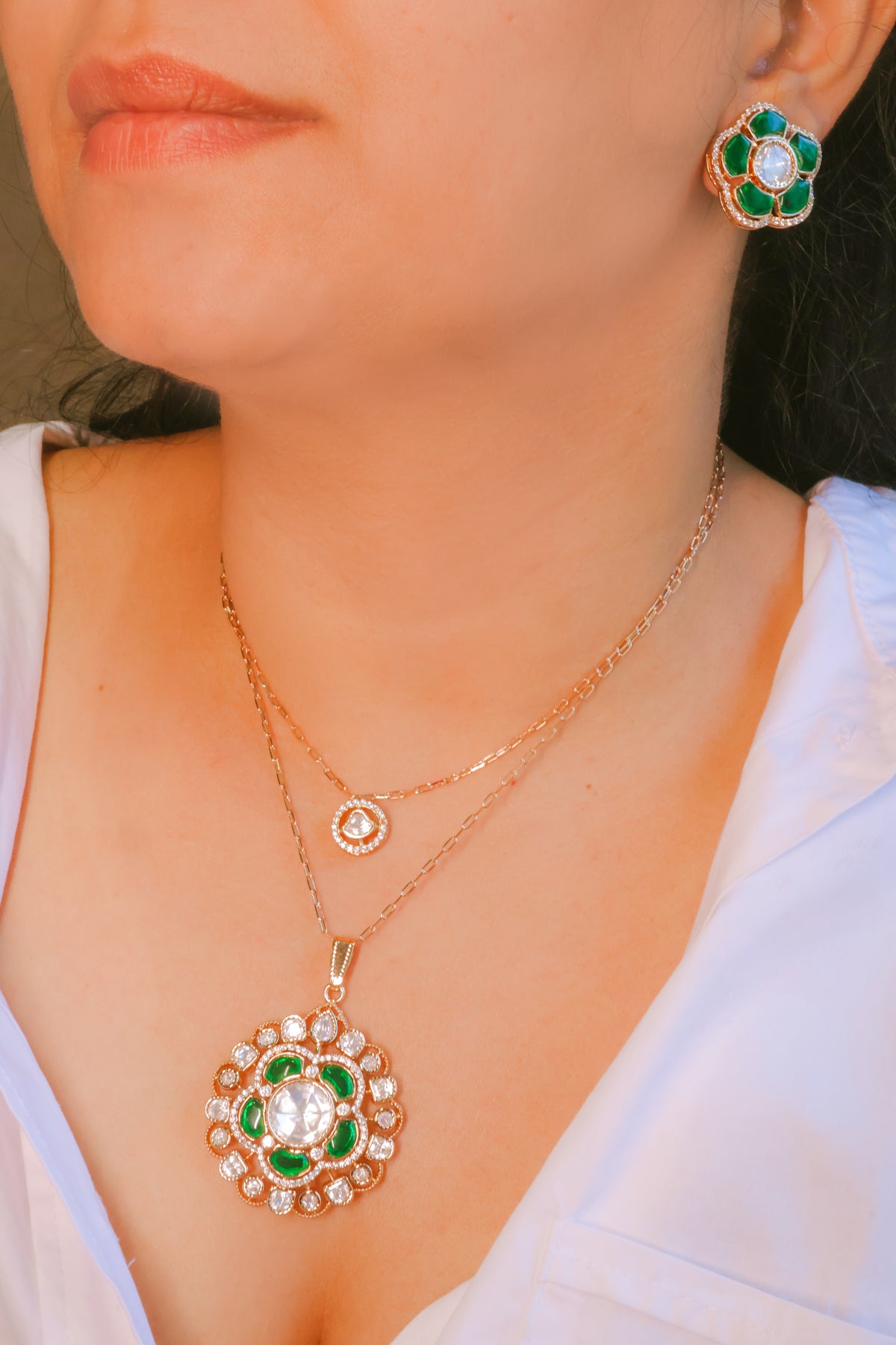 Close-up of a person wearing a gold necklace with a green and white pendant and matching earrings.
