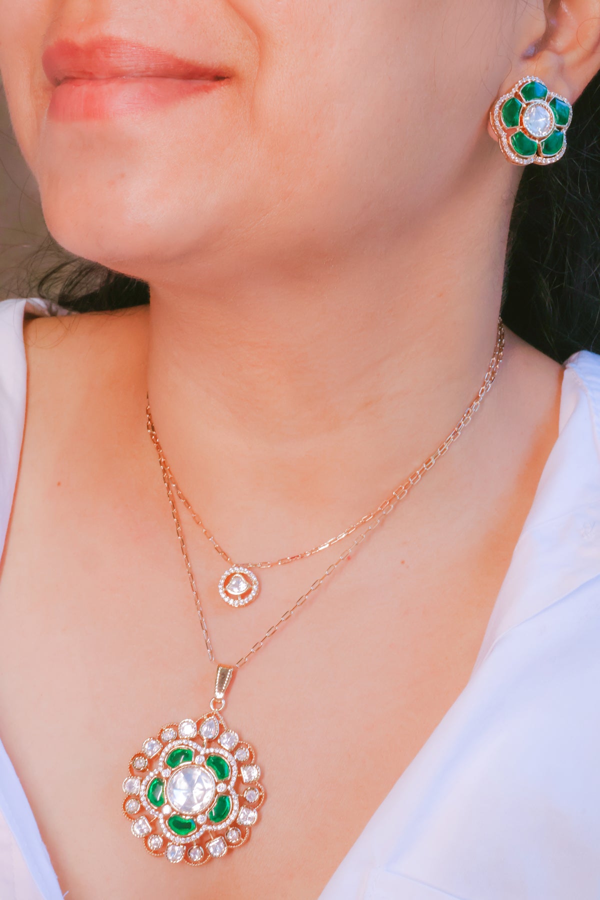 Rose gold necklace and earrings with green gemstones on a person wearing a white top.