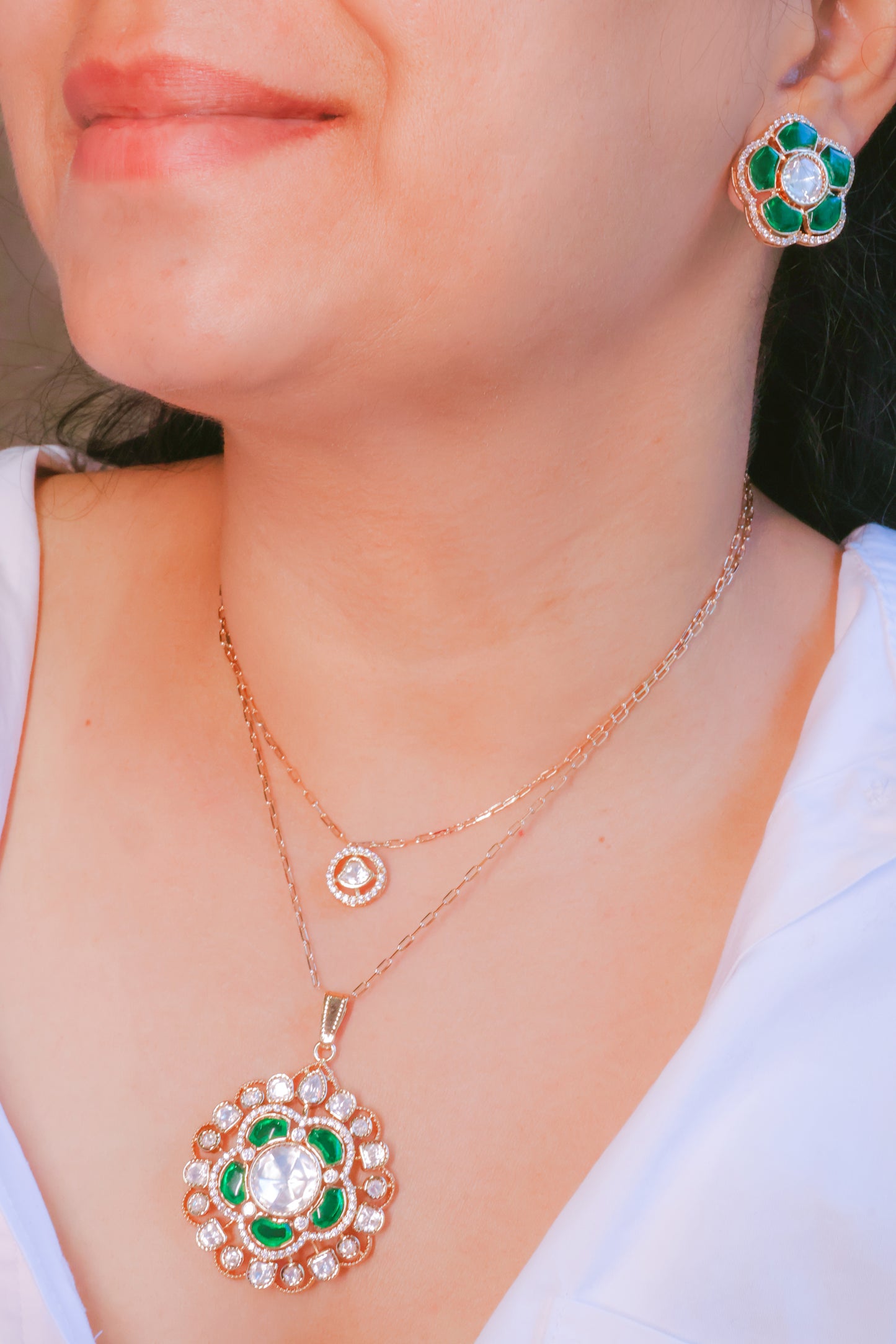 Rose gold necklace and earrings with green gemstones on a person wearing a white top.