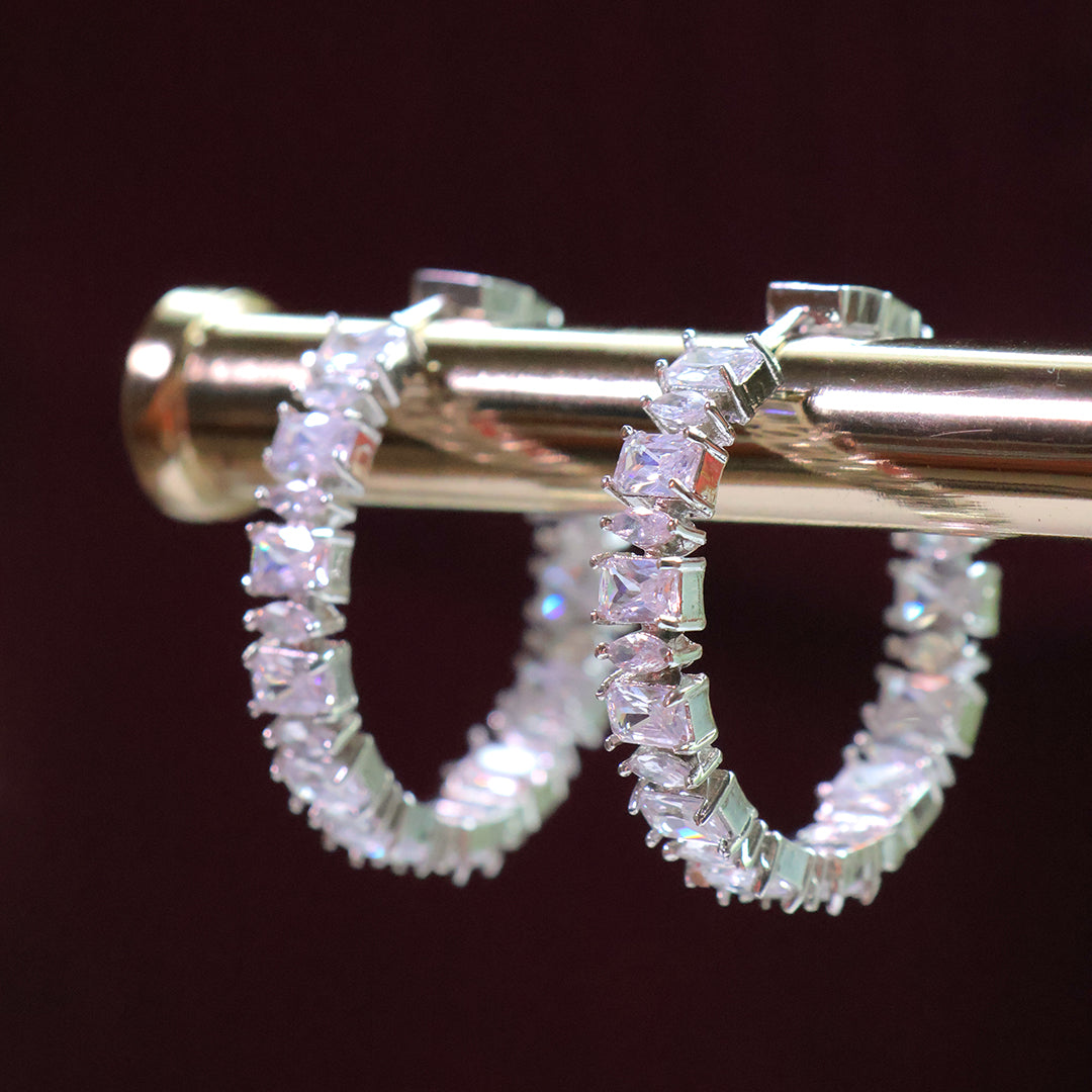 Silver hoop earrings with clear gemstones on a dark background