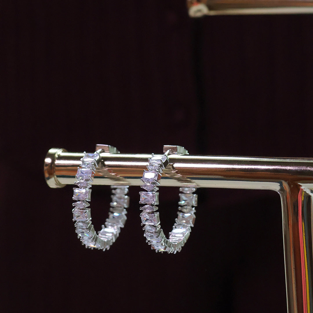 Silver hoop earrings with clear gemstones on a dark background