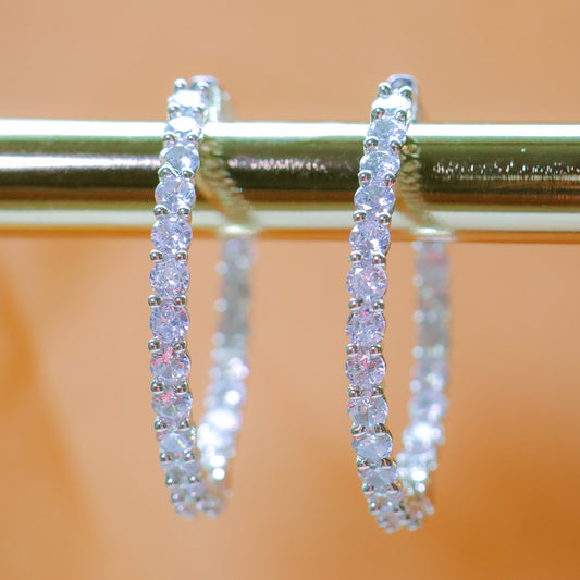 Diamond hoop earrings on a metallic stand with a blurred background